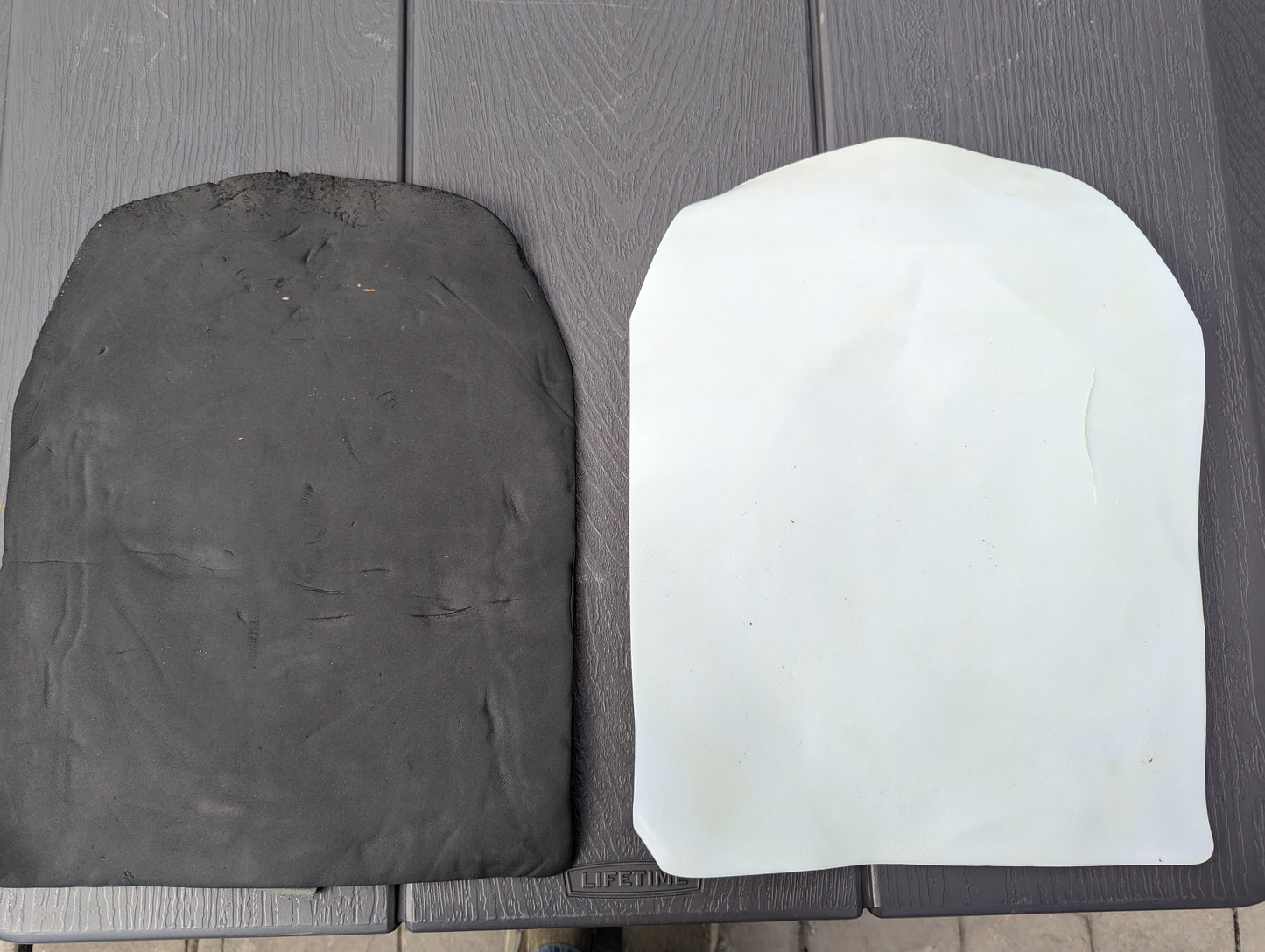 A studio shot showing the two components of the U.S. Military Surplus Assault Pack insert: the black foam comfort pad and the white rigid plastic stiffener, resting on a dark surface.