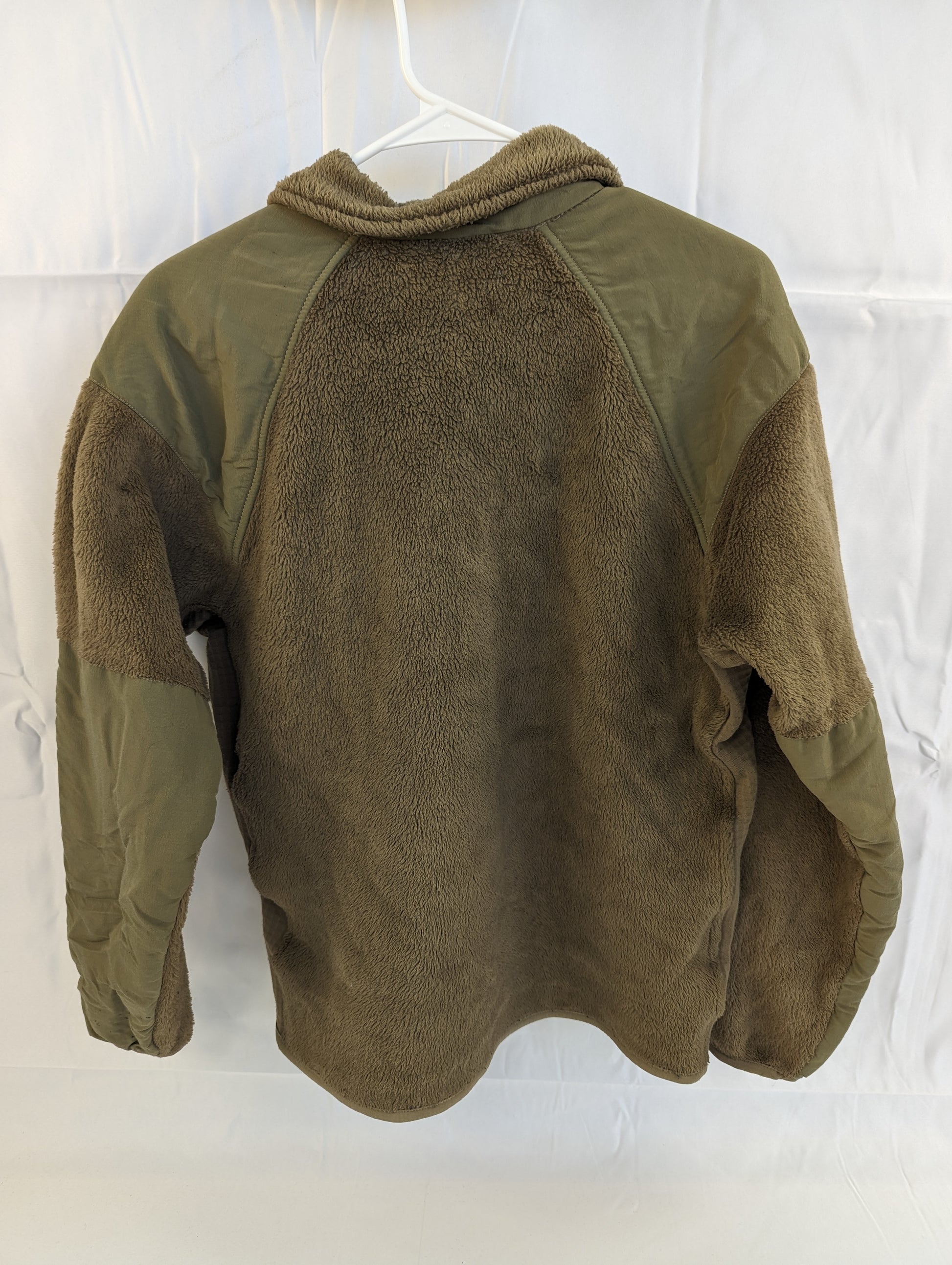 A back view of a U.S. Military Cold Weather Fleece Jacket in Coyote Brown hanging on a hanger, featuring reinforced nylon panels across the shoulders, elbows, and the upper back yoke.