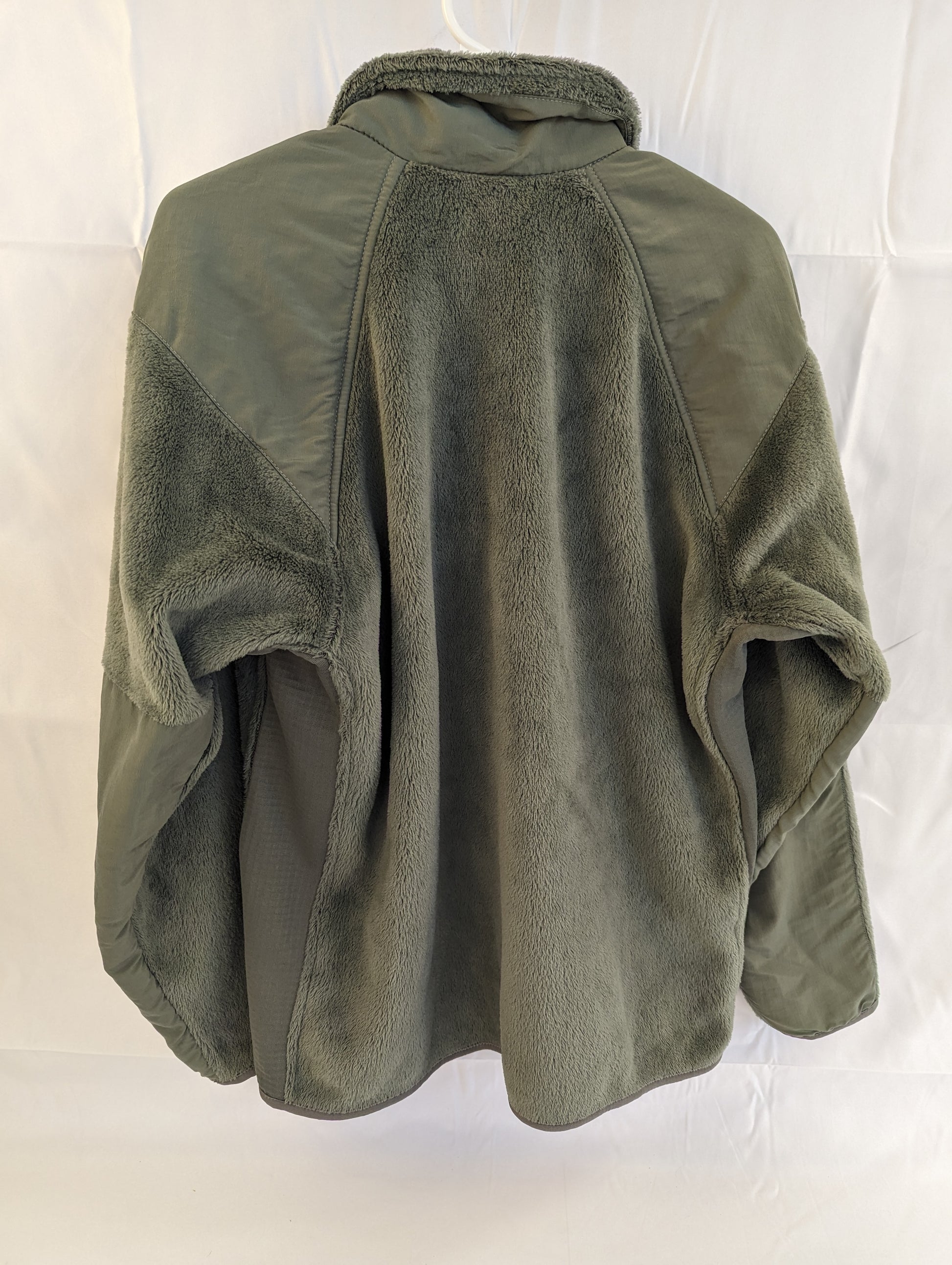 A back view of a U.S. Military Surplus Cold Weather Fleece Jacket in olive green, hanging on a white hanger, highlighting the thick fleece body and reinforced nylon yoke panel on the shoulders.