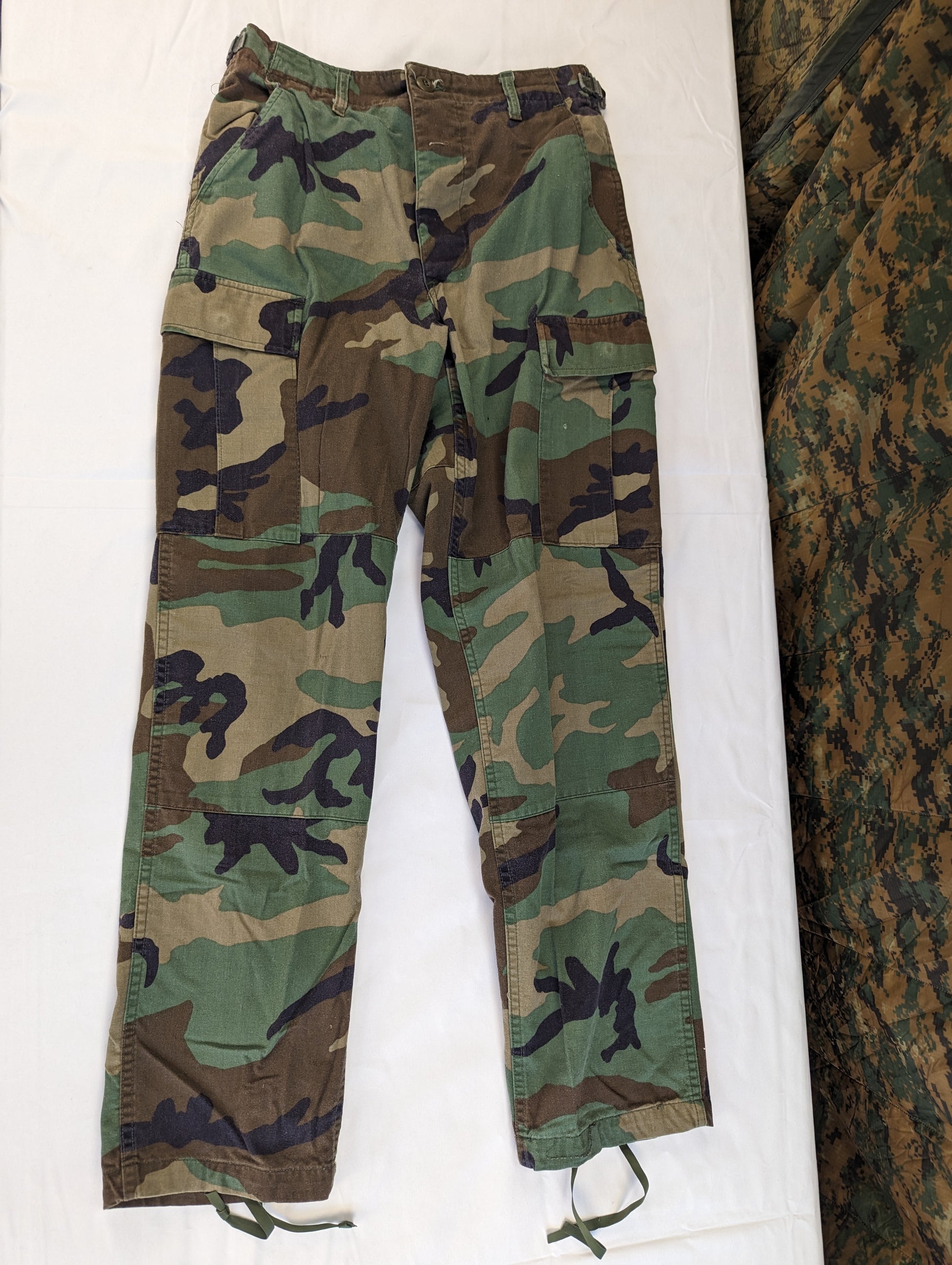 A pair of U.S. Military Surplus Combat Trousers in Woodland camouflage, laid flat and shown from the front, highlighting the cargo pockets and drawstring cuffs.