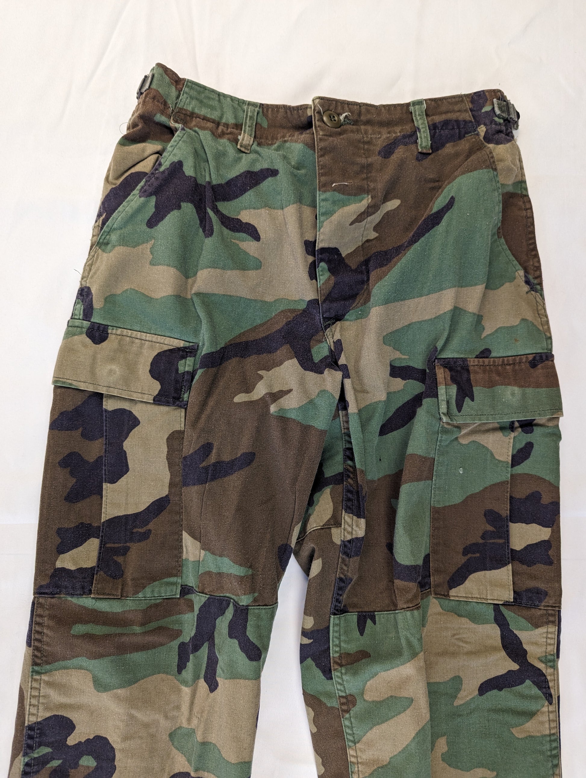 A pair of U.S. Military Surplus Combat Trousers in Woodland camouflage, laid flat and shown from the front, highlighting the waistline, front pockets, and large cargo pockets.