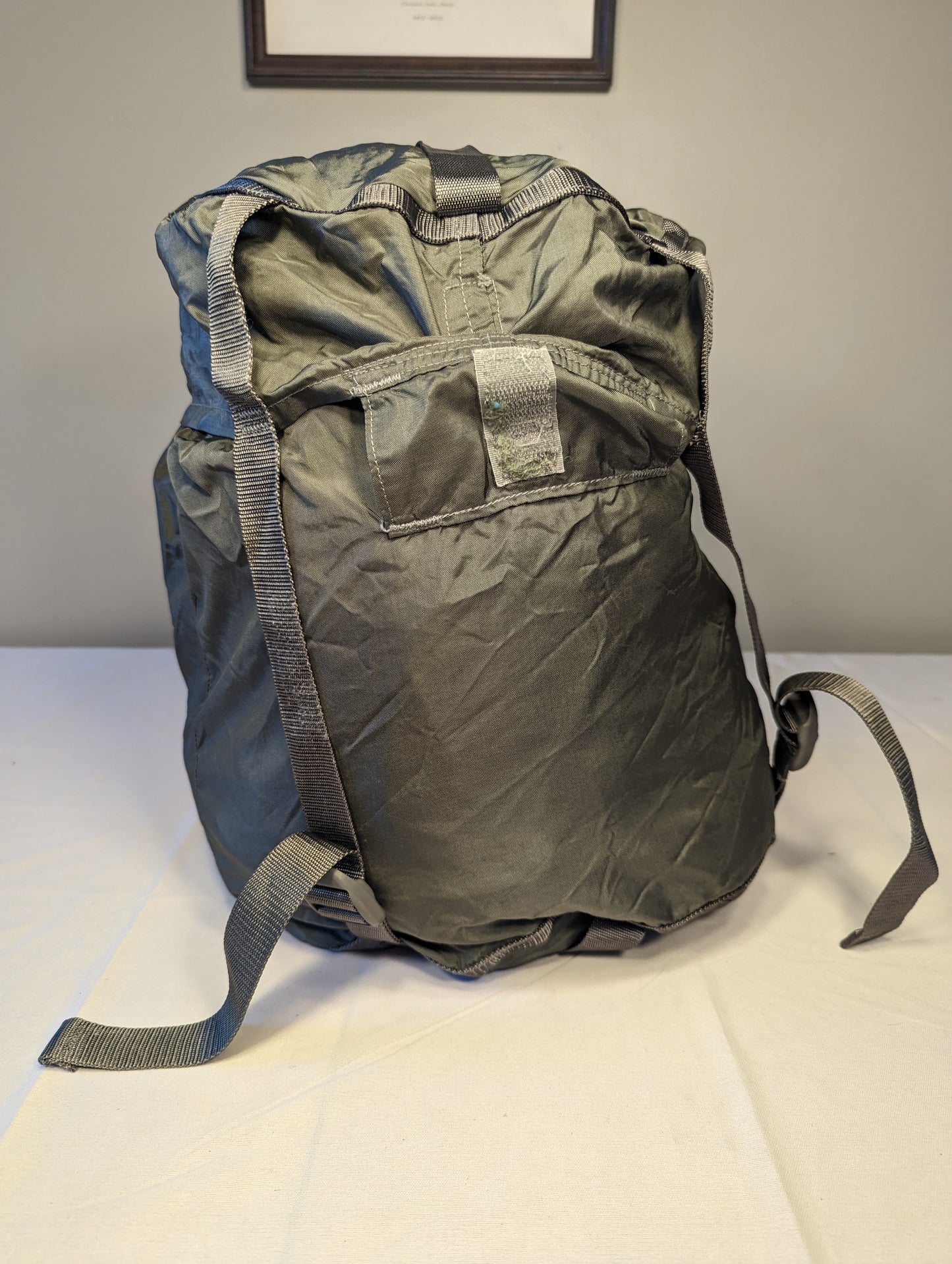A large, packed U.S. Military Surplus Compression Stuff Sack in foliage green, standing upright on a white surface, highlighting the unique wavy quilted texture and thick compression straps.