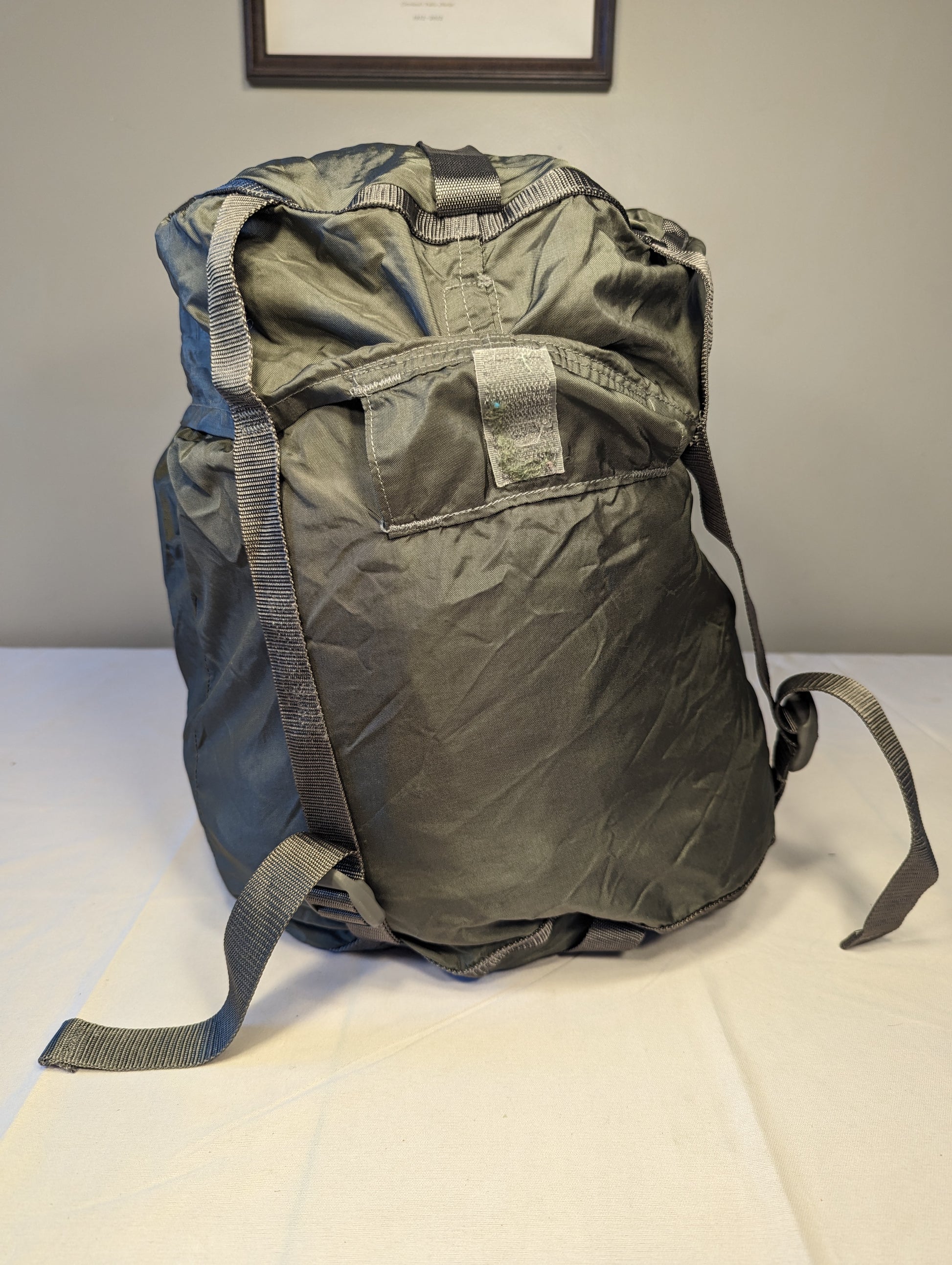 A large, packed U.S. Military Surplus Compression Stuff Sack in foliage green, standing upright on a white surface, highlighting the unique wavy quilted texture and thick compression straps.