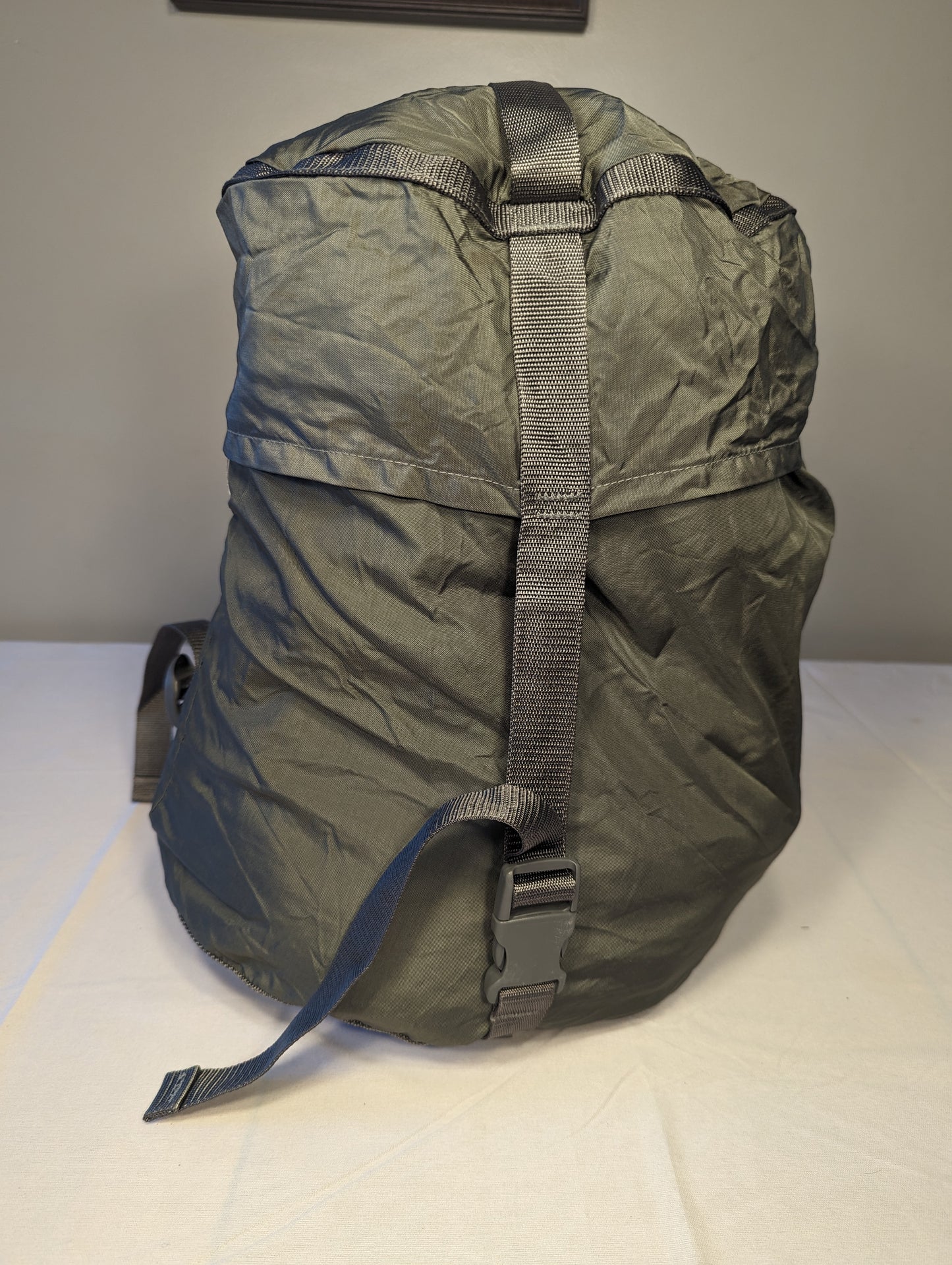 A large, tightly compressed U.S. Military Surplus Compression Stuff Sack in foliage green, standing upright, featuring heavy-duty webbing straps and a distinct wrinkled nylon texture.