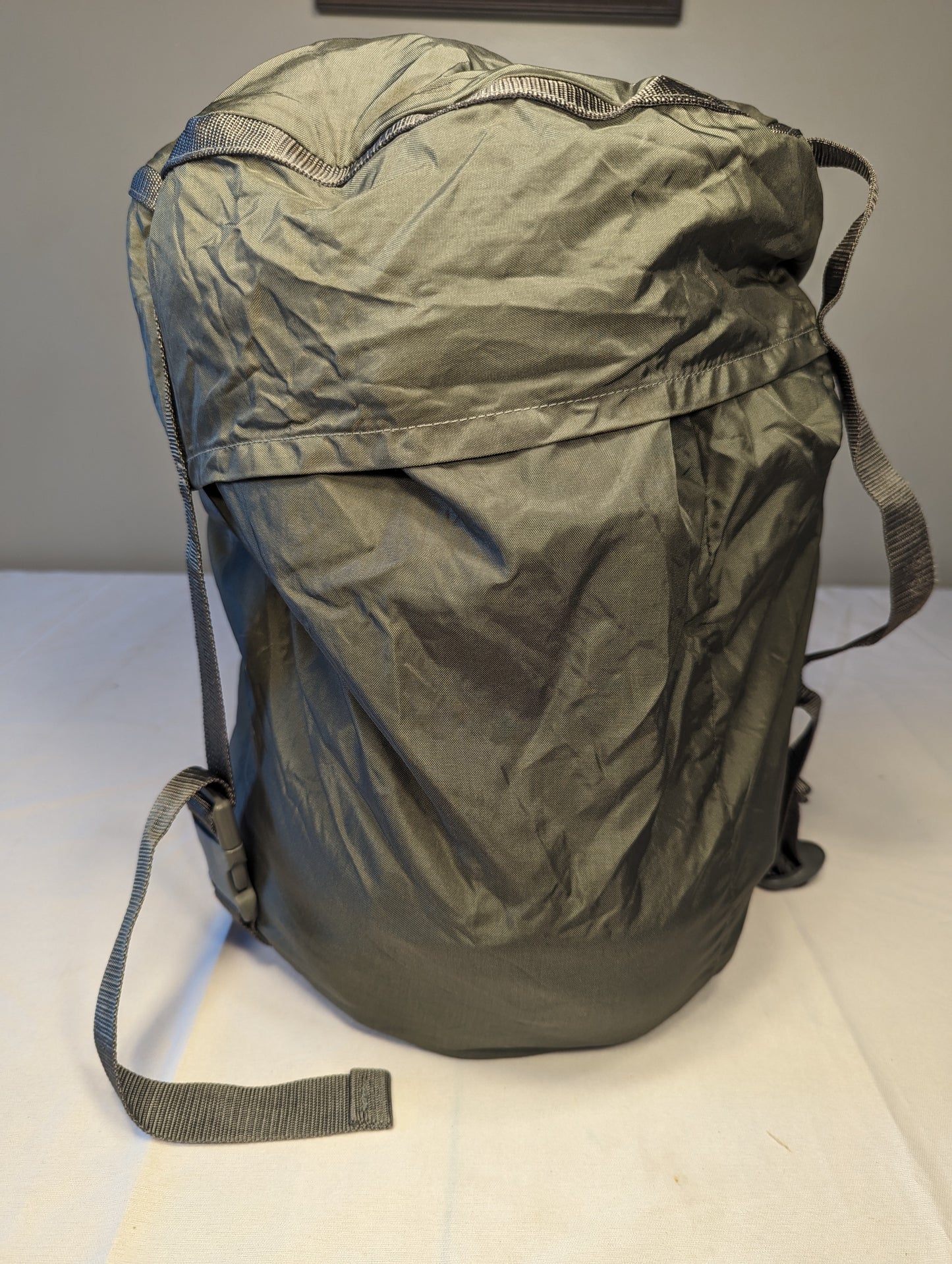 A large U.S. Military Surplus Compression Stuff Sack in foliage green, standing upright, featuring heavy-duty webbing straps and a distinctive wavy quilted fabric texture.