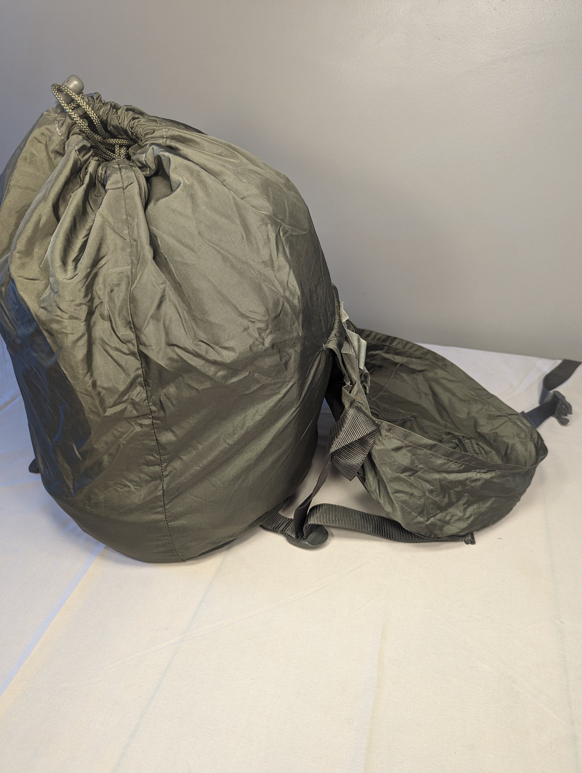 A small U.S. Military Surplus stuff sack in dark olive green, fully packed and cinched closed with drawstrings, displayed on a light-colored surface.