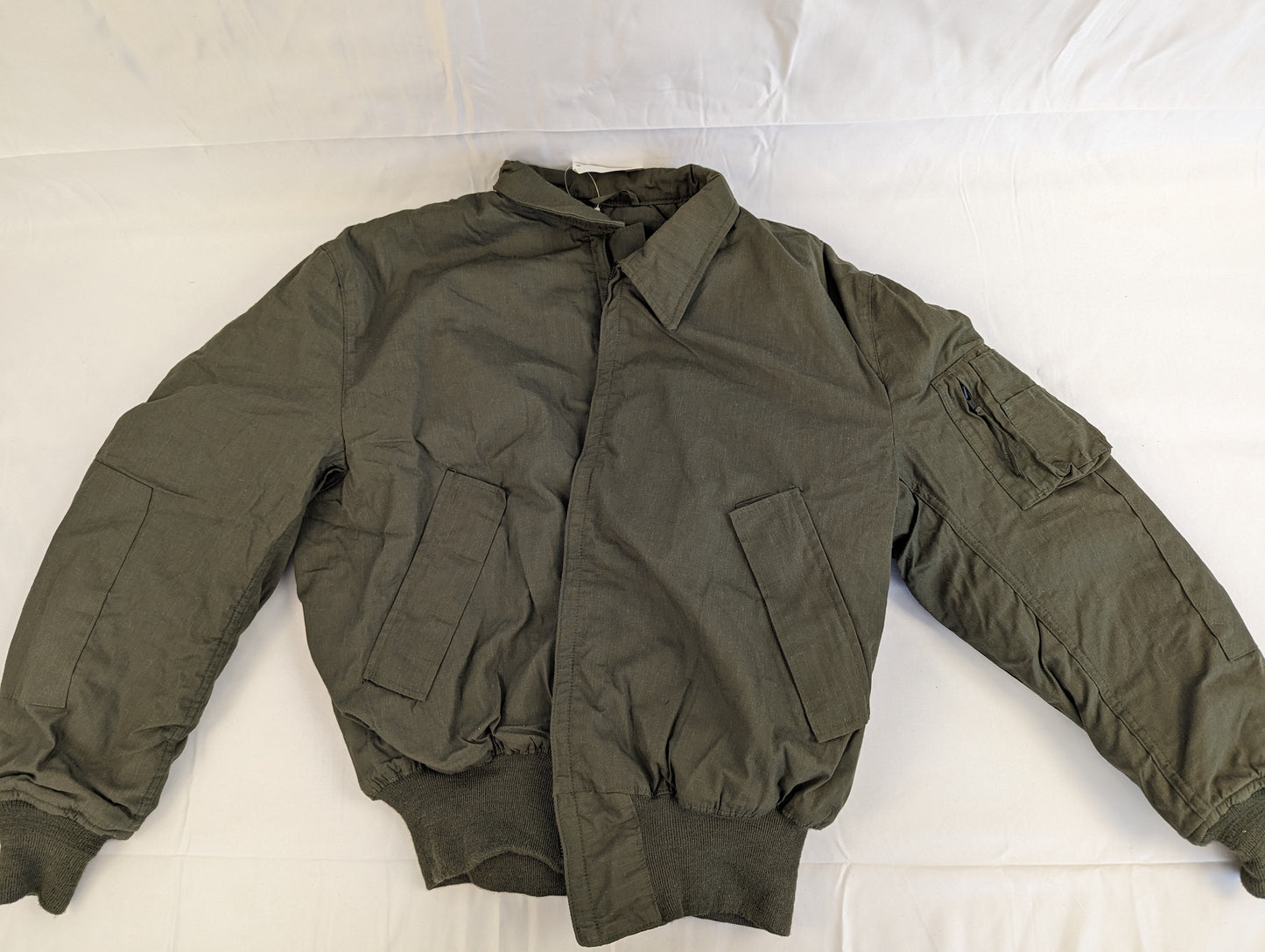 A full front view of a U.S. Military Cold Weather Combat Vehicle Crew (CVC) jacket in olive green, laid flat on a white background, highlighting the zippered chest pockets and ribbed cuffs.