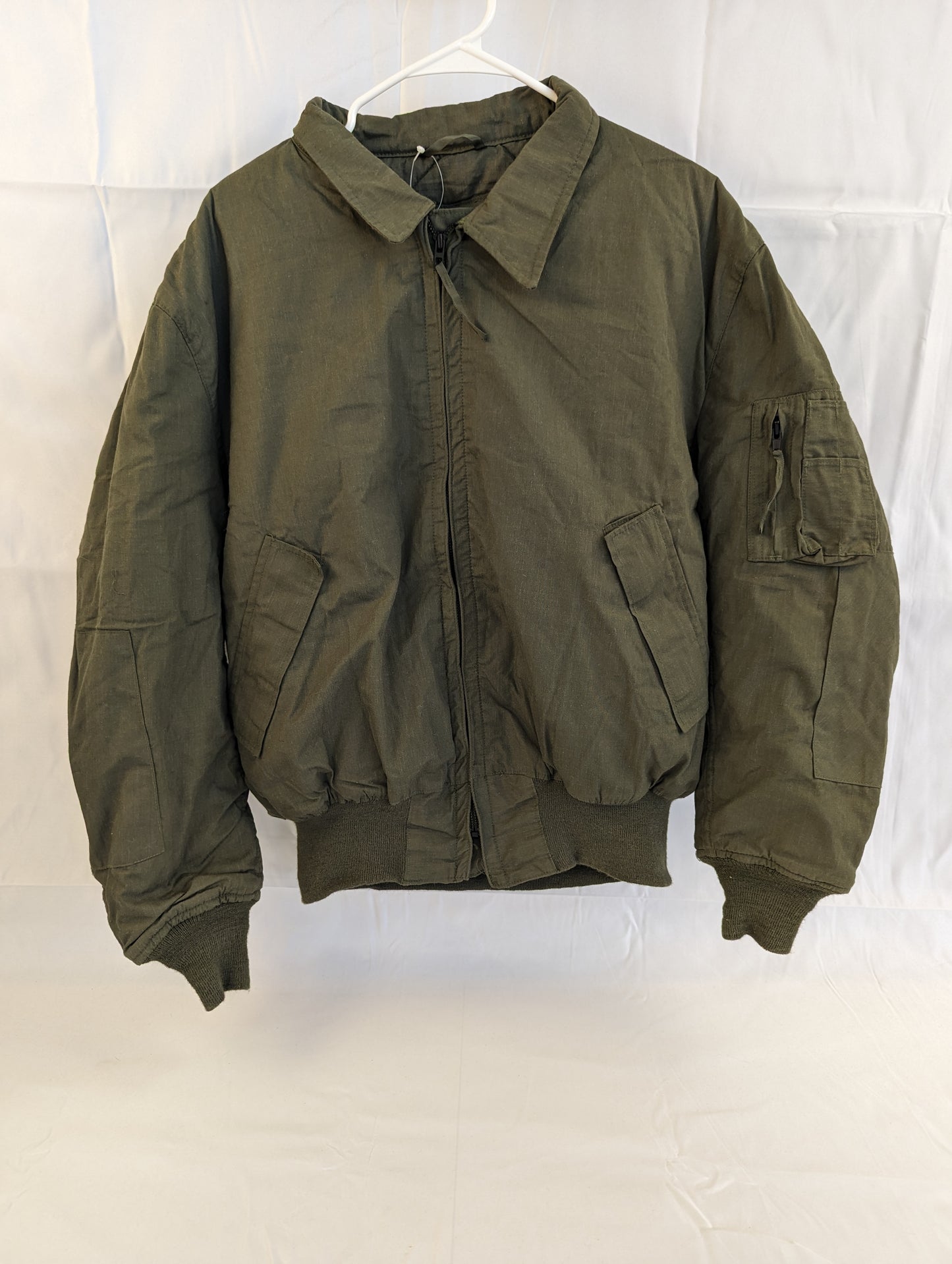 A front view of a U.S. Military Cold Weather Combat Vehicle Crew (CVC) jacket in olive green, featuring a zippered front, ribbed cuffs, and angled chest pockets, hanging on a white background.