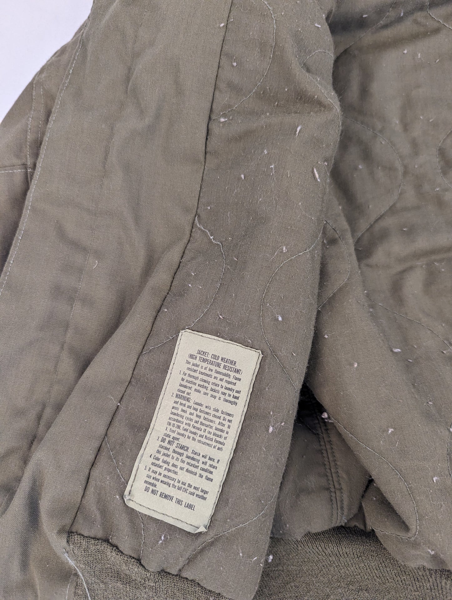 A close-up of the quilted olive green lining of the U.S. Military CVC jacket, highlighting the diamond stitch pattern and a faded, worn military issue tag.
