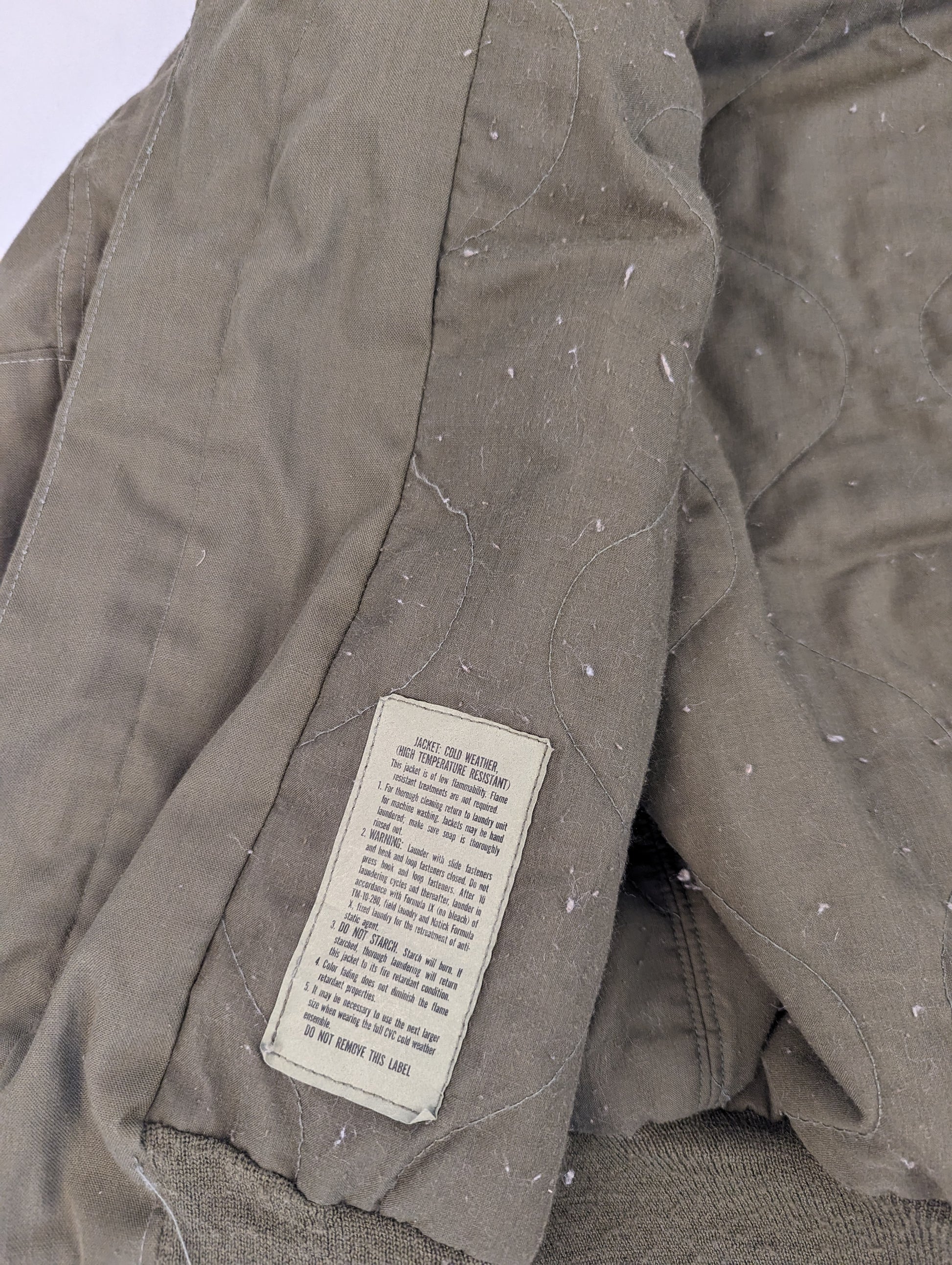 A close-up of the quilted olive green lining of the U.S. Military CVC jacket, highlighting the diamond stitch pattern and a faded, worn military issue tag.