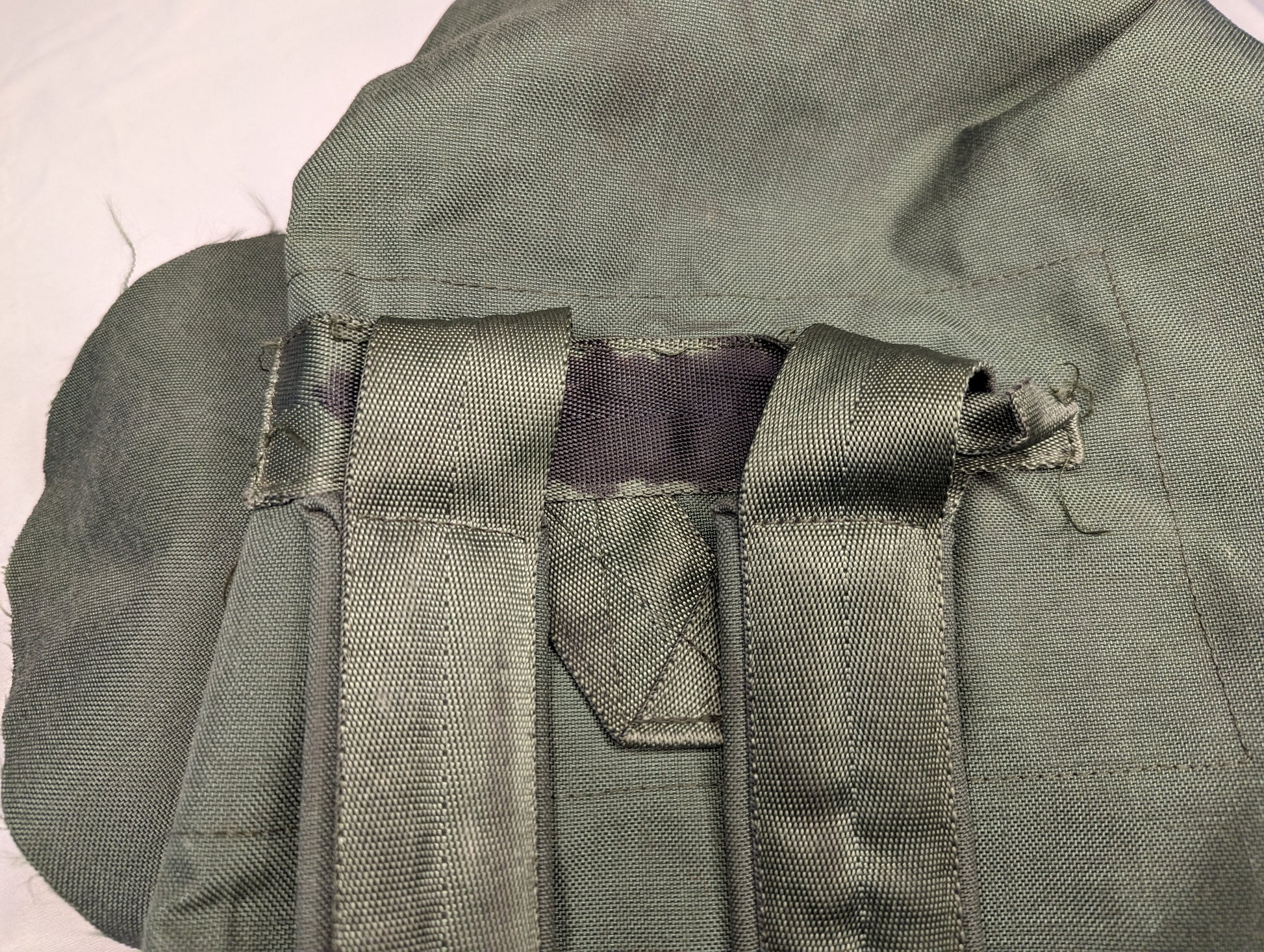 An extreme close-up of the olive green U.S. Military Duffel Bag, highlighting a damaged carry handle attachment point with frayed webbing and a tear in the main fabric.
