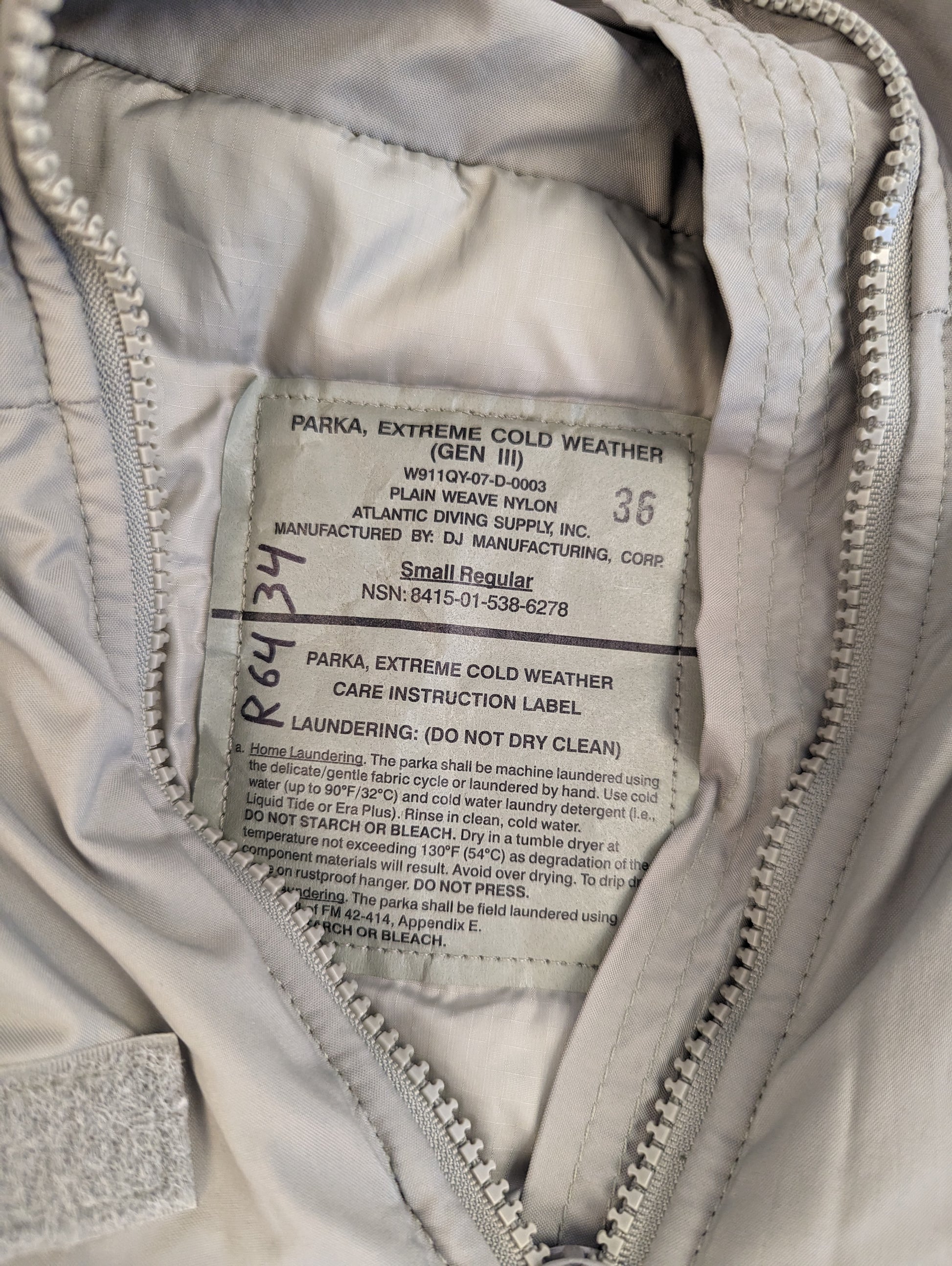 A close-up photograph of the official U.S. Military issue tag sewn into the Extreme Cold Weather Parka (Gen III), displaying the product name, NSN 8415-01-538-6778, and detailed care instructions.