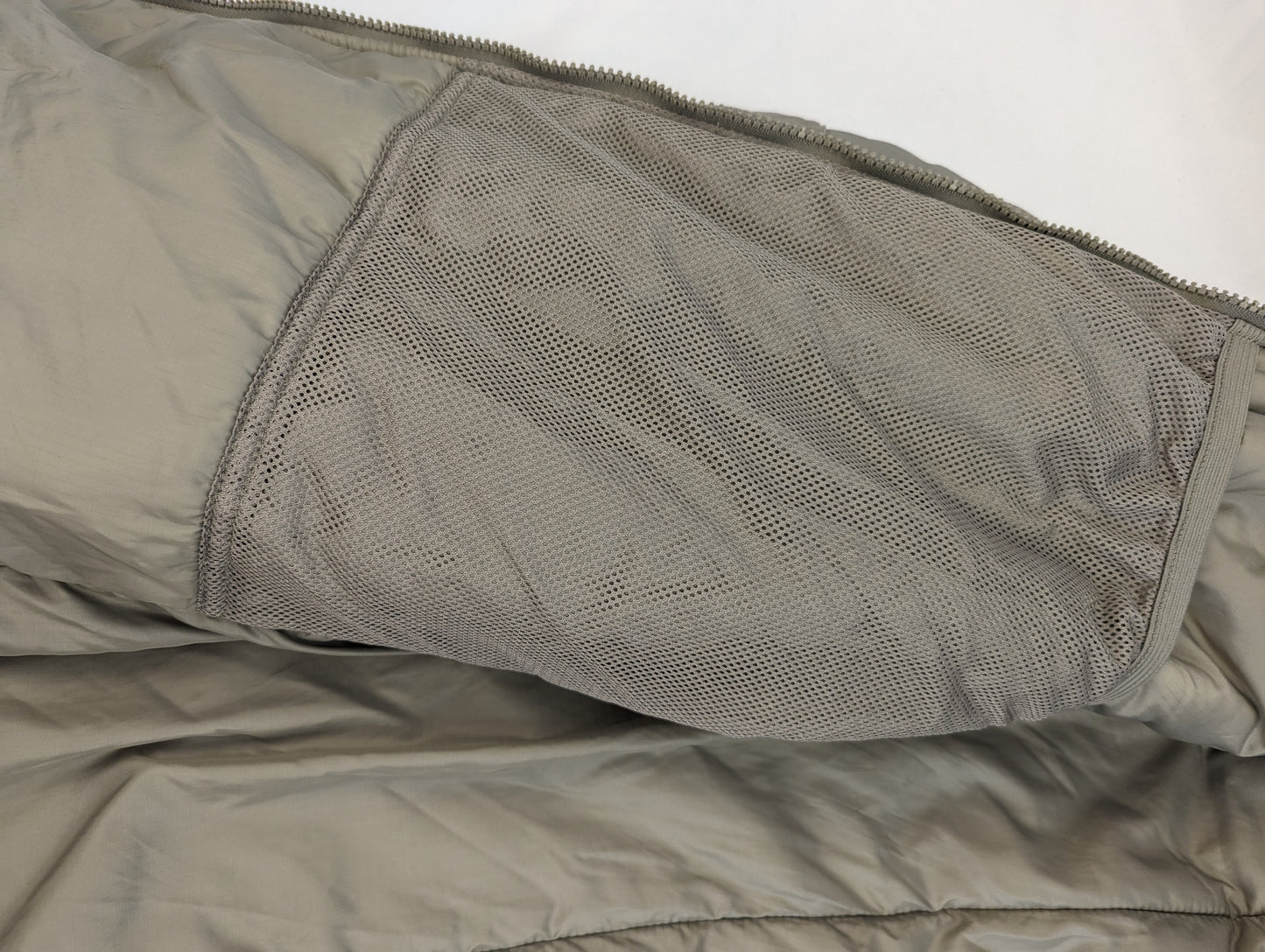 A close-up view of the interior of the U.S. Military Extreme Cold Weather Parka, highlighting the large, open mesh storage pocket sewn into the quilted lining.