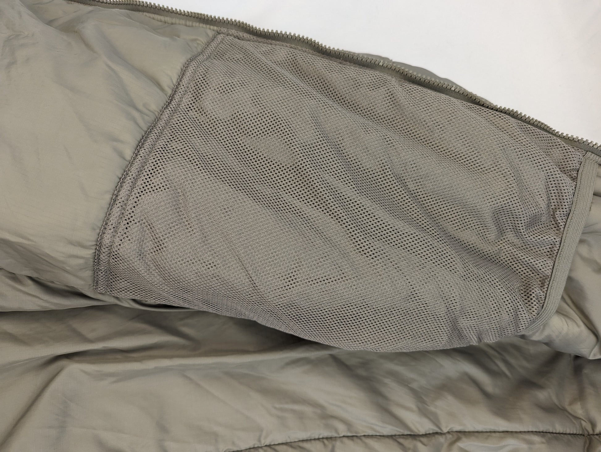 A close-up view of the interior of the U.S. Military Extreme Cold Weather Parka, highlighting the large, open mesh storage pocket sewn into the quilted lining.