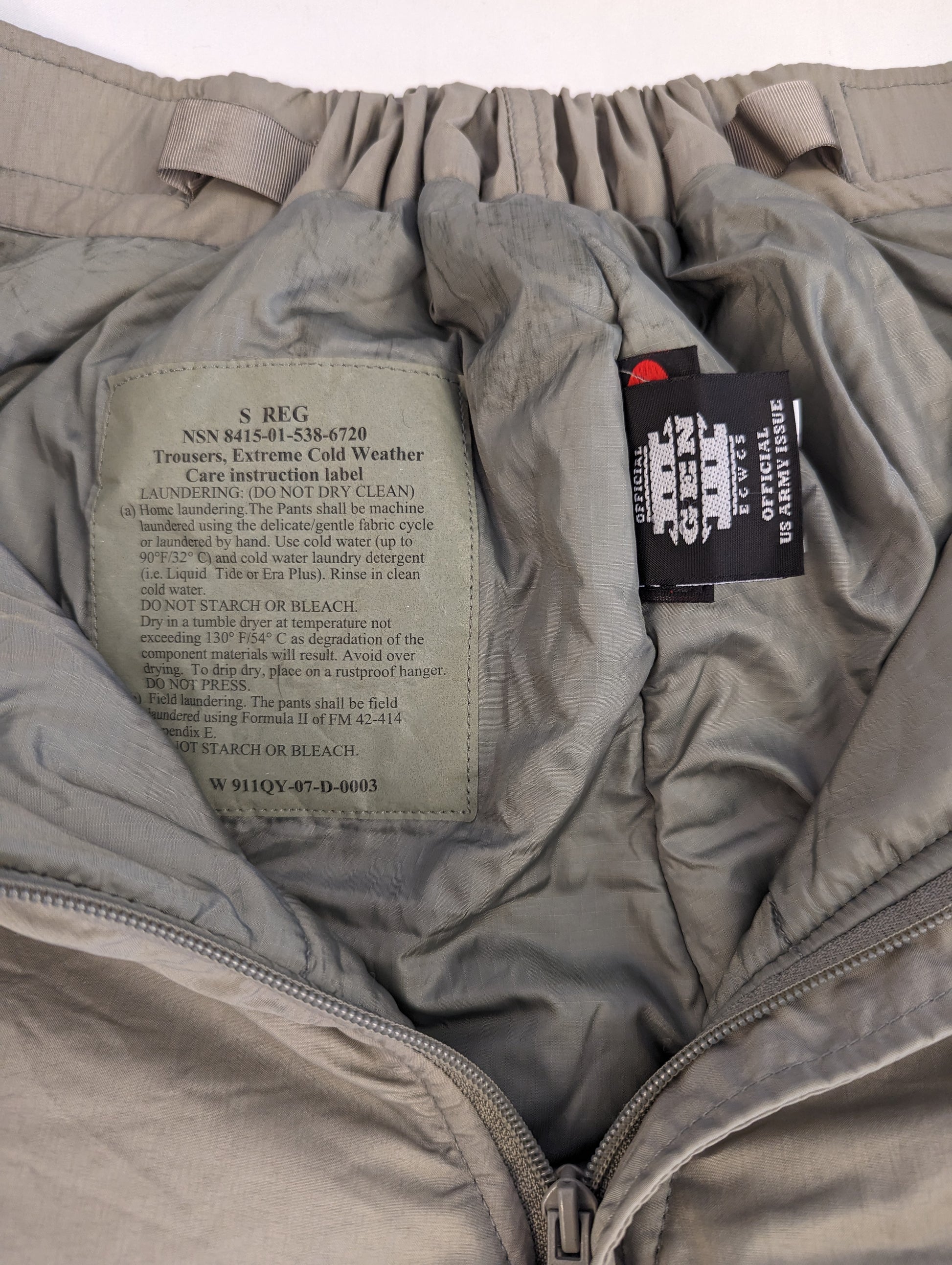 A close-up view of the interior waistband of the U.S. Military Extreme Cold Weather Trousers, displaying the size and issue tag (S REG, NSN 8415-01-534-4178) and the 'MADE WITH PRIMALOFT' insulation tag.