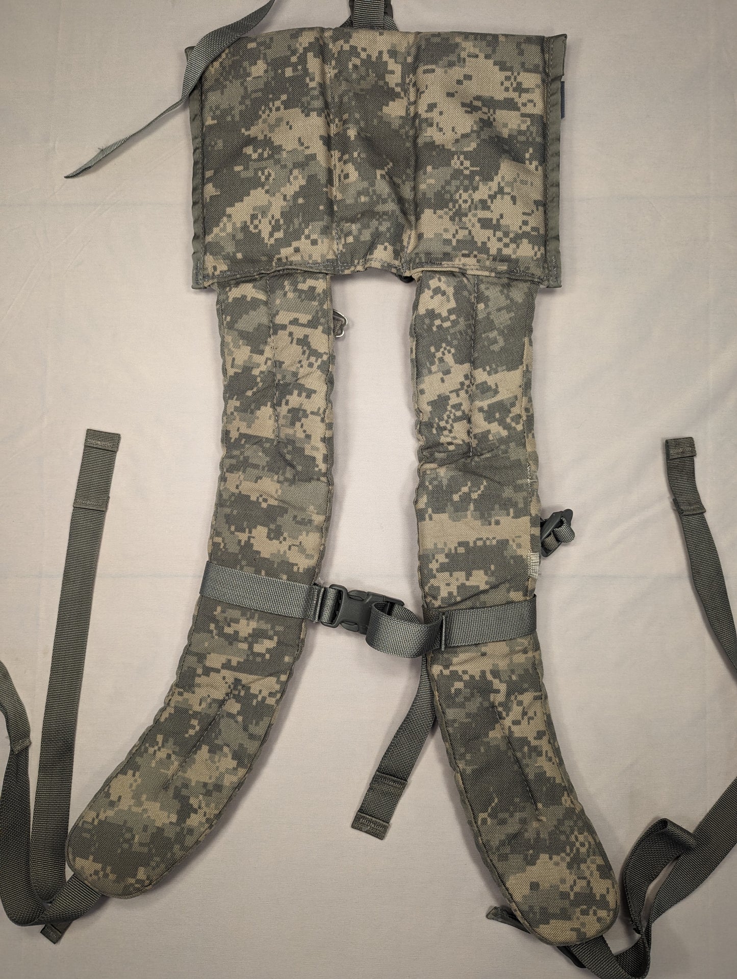 A close-up, overhead view of a pair of U.S. Military Surplus Enhanced Frame Shoulder Straps in ACU digital camouflage, laid flat to display the thick padding, yoke panel, and black adjustment buckles.