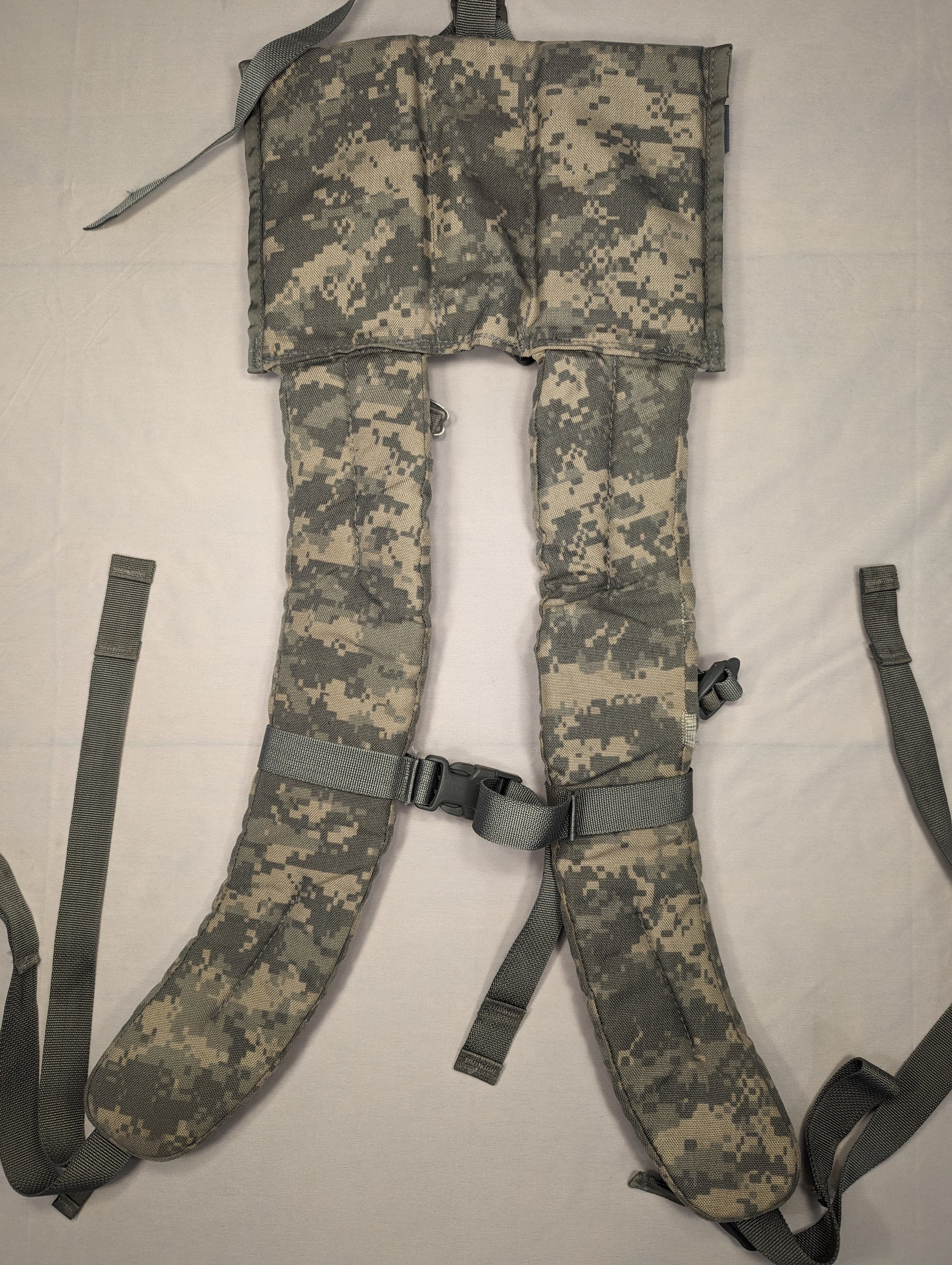 A close-up, overhead view of a pair of U.S. Military Surplus Enhanced Frame Shoulder Straps in ACU digital camouflage, laid flat to display the thick padding, yoke panel, and black adjustment buckles.