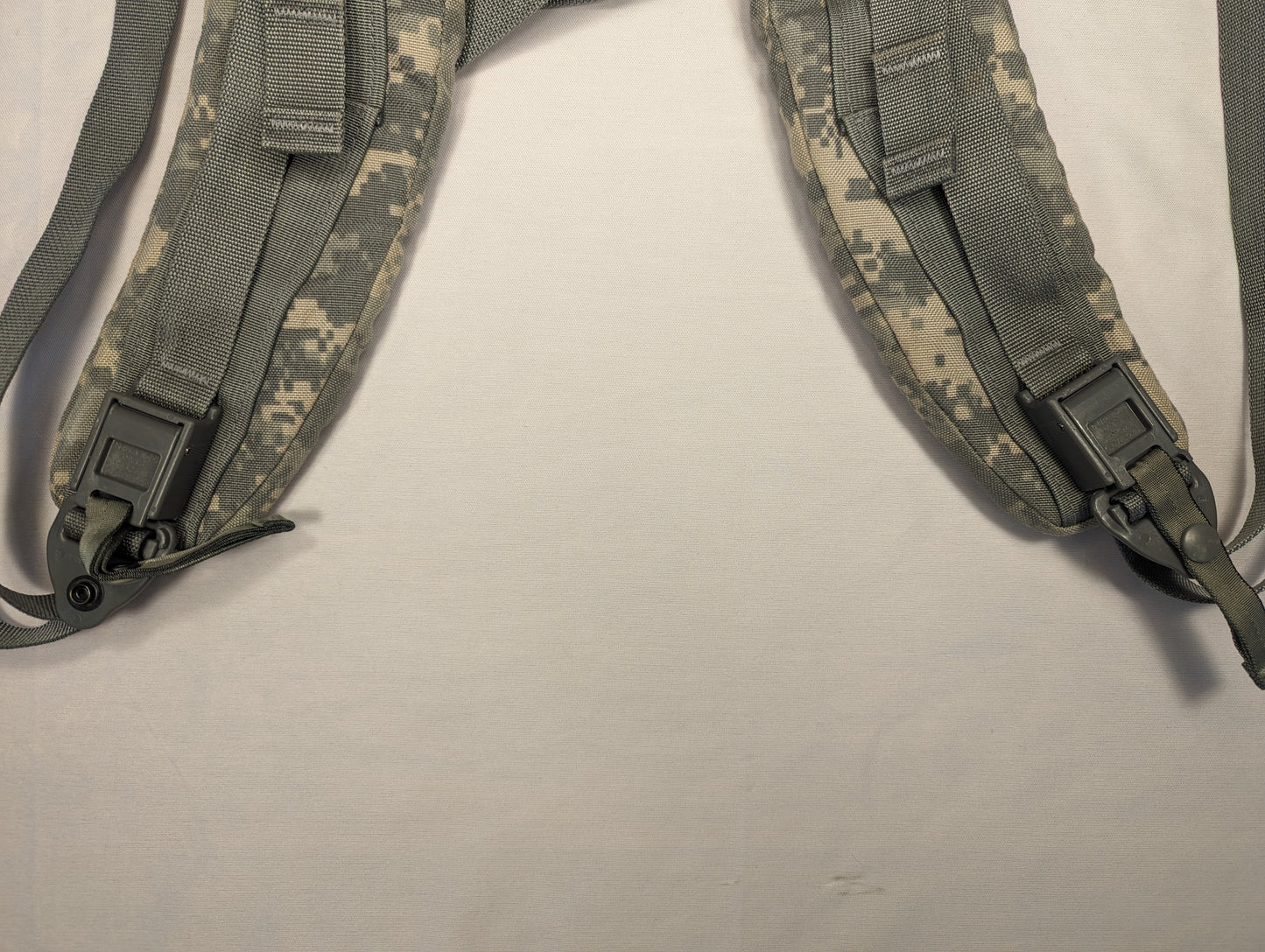 A close-up view of a pair of U.S. Military Surplus Enhanced Frame Shoulder Straps in ACU digital camouflage, laid out in a V-shape, highlighting the padded construction, plastic buckles, and D-ring attachments.