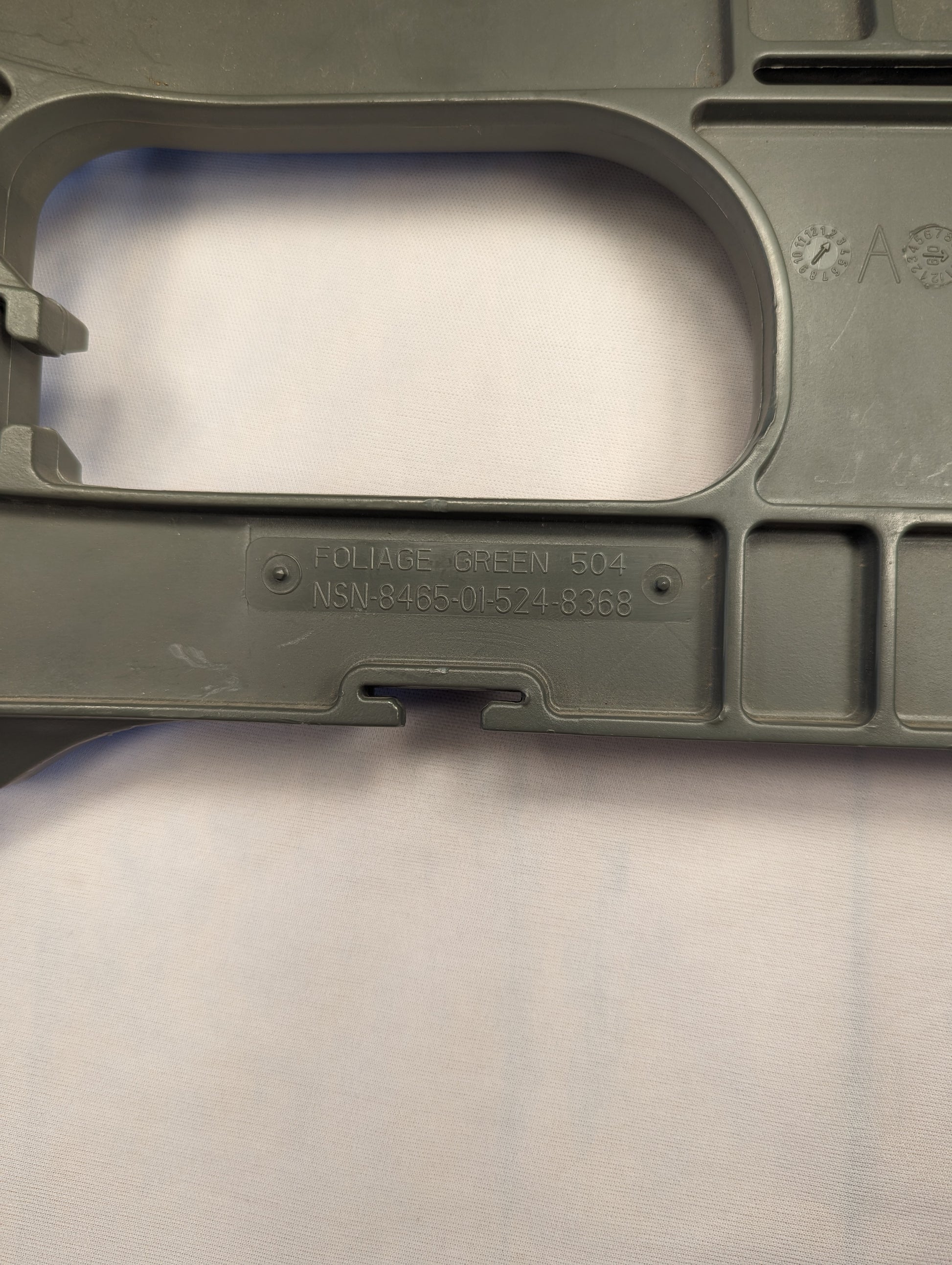 A close-up photograph of the olive green plastic frame of a U.S. Military Enhanced Rucksack Frame, clearly displaying the embossed text 'PAT. PEND.' and the National Stock Number (NSN) 8465-01-519-8389.