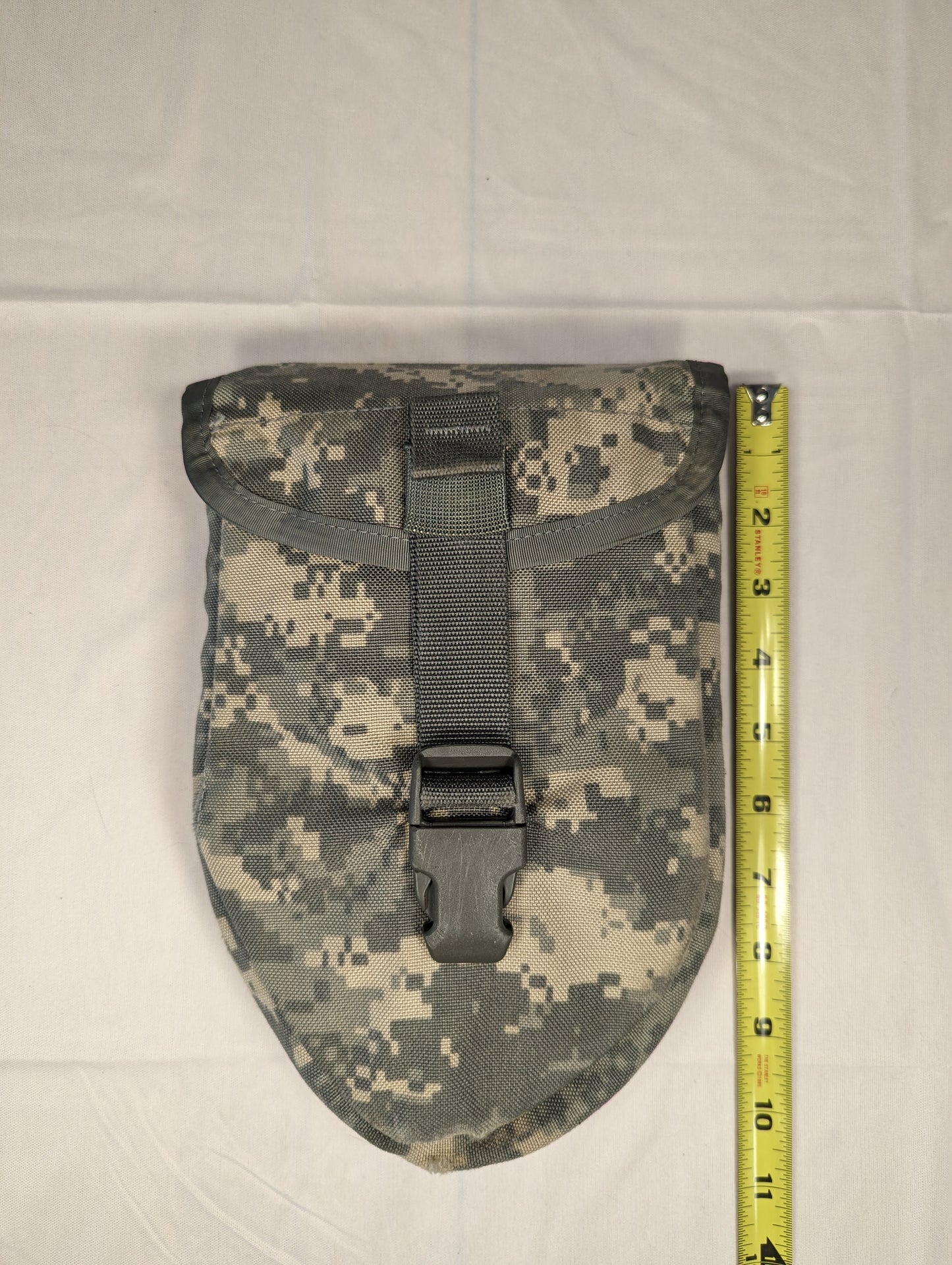 A single U.S. Military Surplus Entrenching Tool Carrier pouch in ACU digital camouflage, standing upright next to a yellow tape measure to demonstrate its height, with the flap secured by a black quick-release buckle.