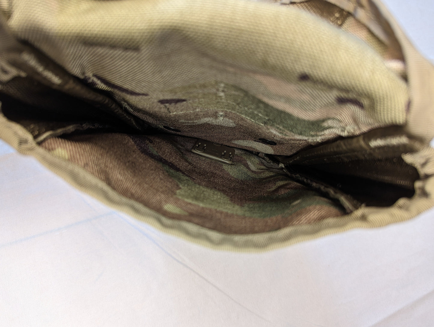 A very close-up, high-angle view looking deep inside the empty OCP/Multicam Entrenching Tool Carrier pouch, highlighting the wrinkled camouflage interior fabric.