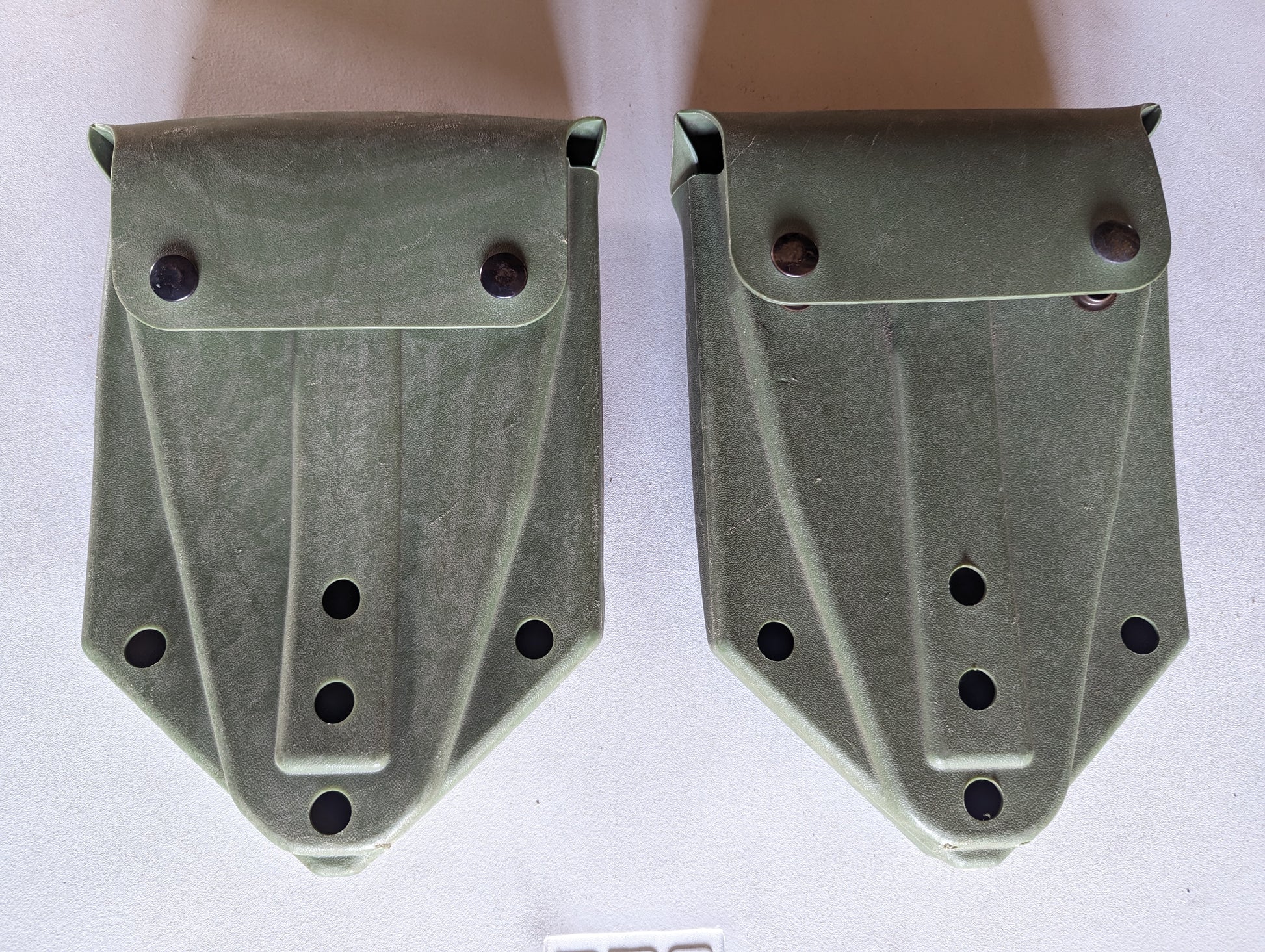 Two U.S. Military Surplus plastic entrenching tool carrier cases in olive drab green, laid side-by-side, featuring snap-button flap closures and a rugged molded design.