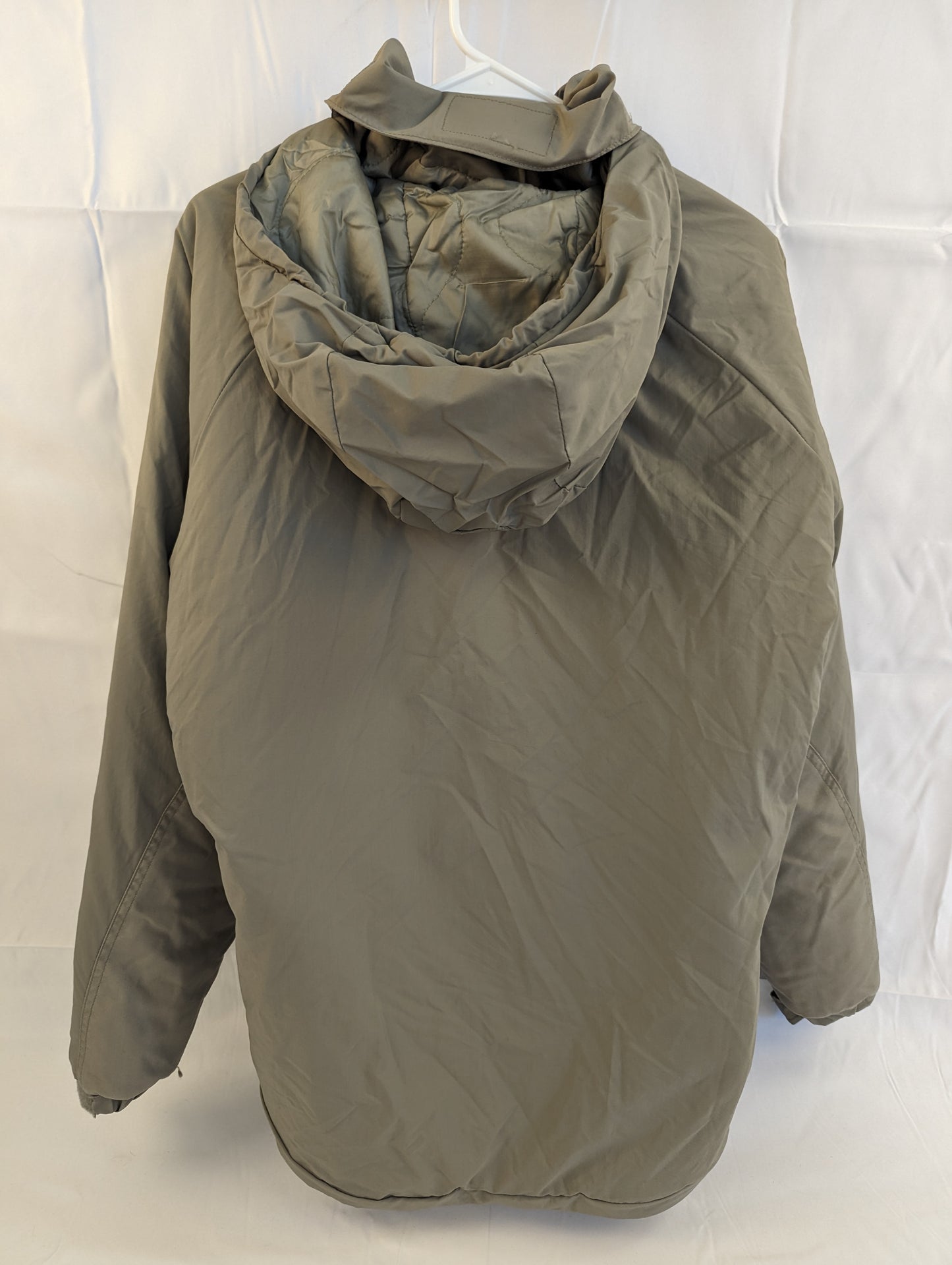 A back view of a U.S. Military Extreme Cold Weather Parka in gray/foliage green, hanging on a white hanger, highlighting the bulky, quilted insulation and high collar with a stowed hood.