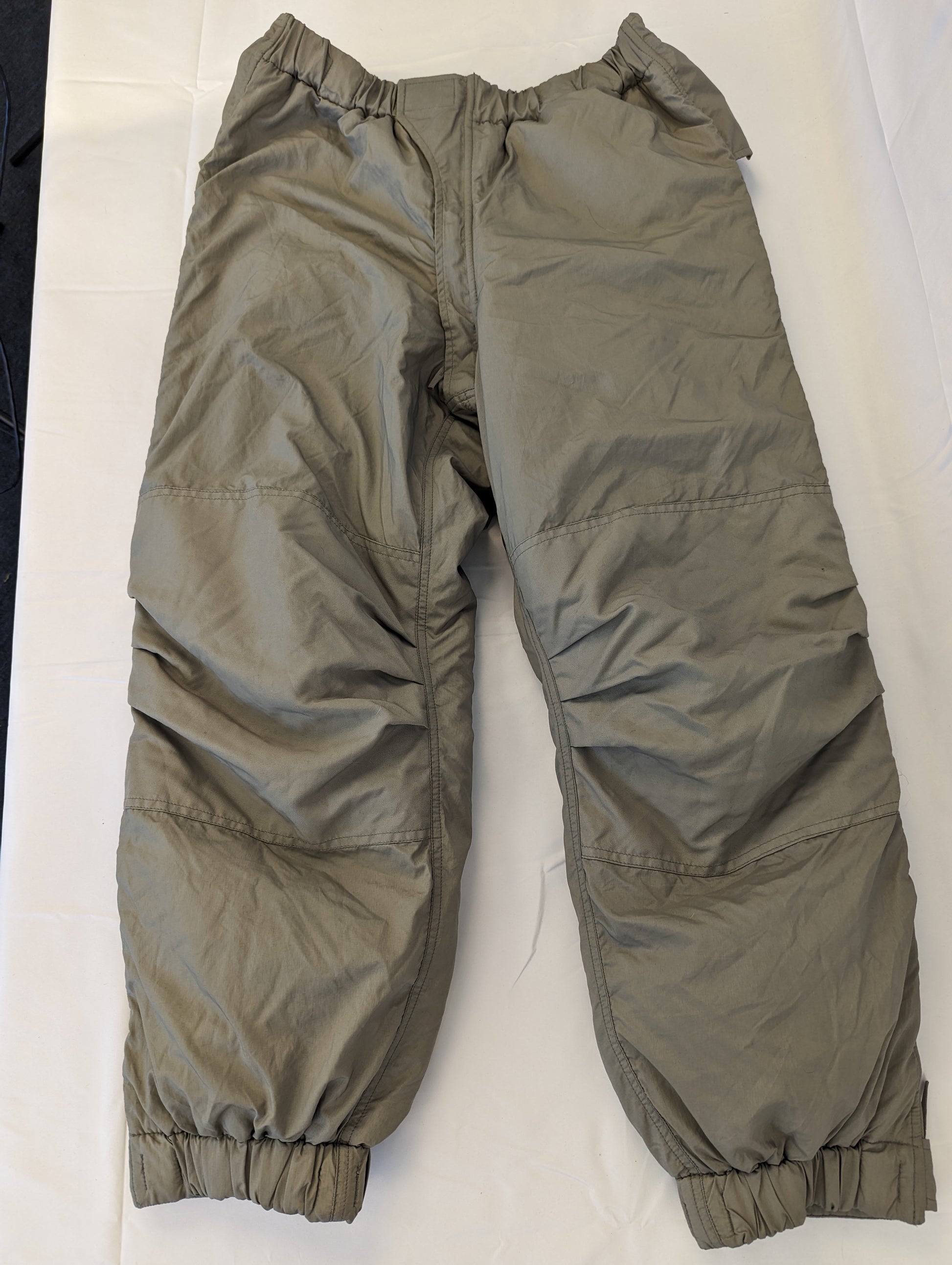A full-length view of U.S. Military Surplus Extreme Cold Weather Trousers in gray, laid flat, featuring bulky, quilted insulation, reinforced knee patches, and elastic cuffs.