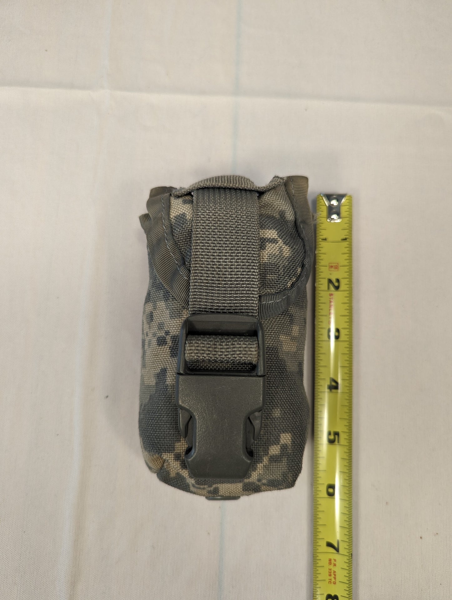 A single U.S. Military Surplus FG Pouch in ACU digital camouflage, standing upright next to a yellow tape measure to demonstrate its height, featuring a black quick-release buckle closure.