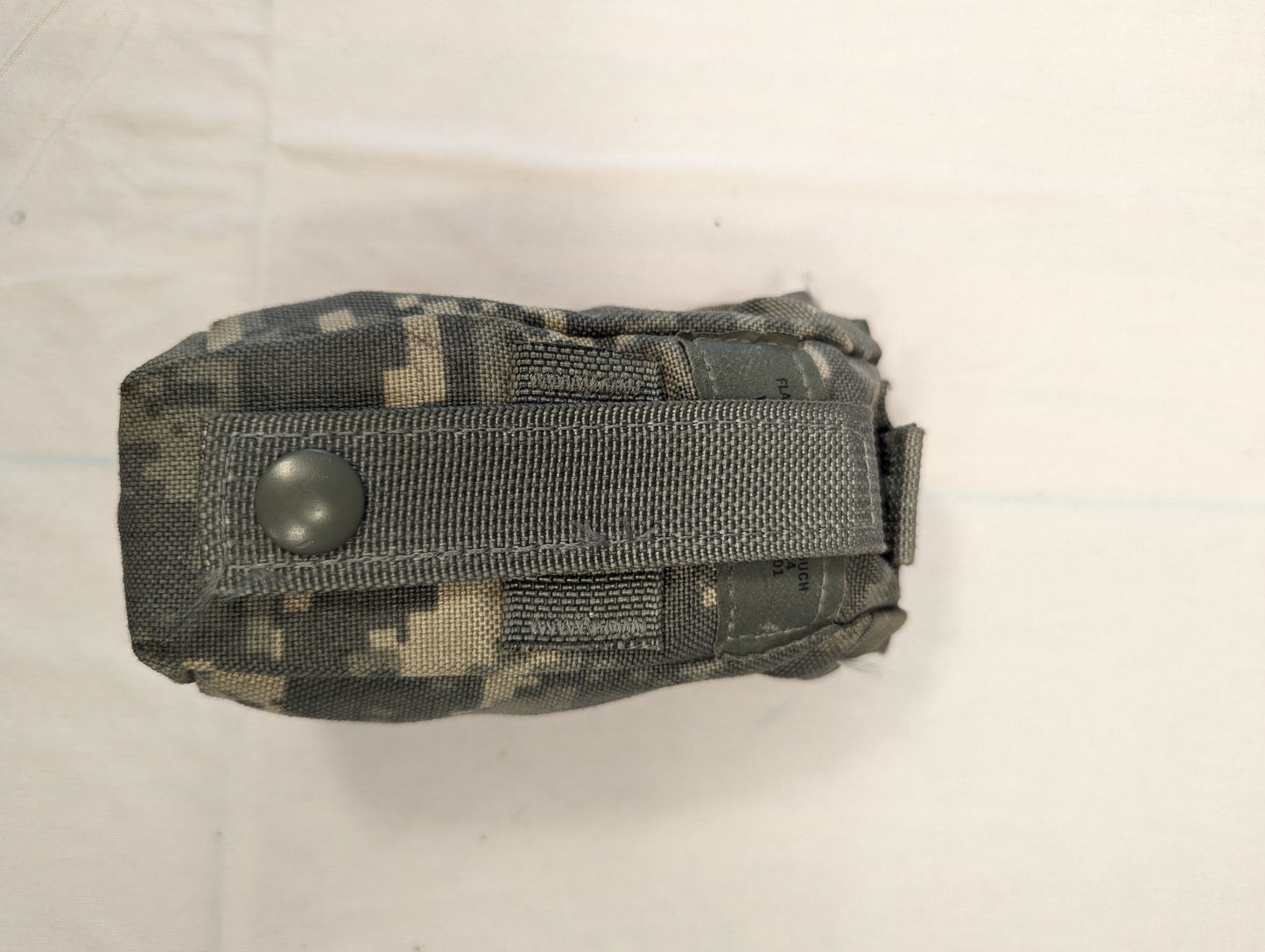 A single U.S. Military Surplus small pouch in ACU digital camouflage, laid flat, secured by a large horizontal gray webbing strap with a black snap button closure, and featuring MOLLE webbing loops.