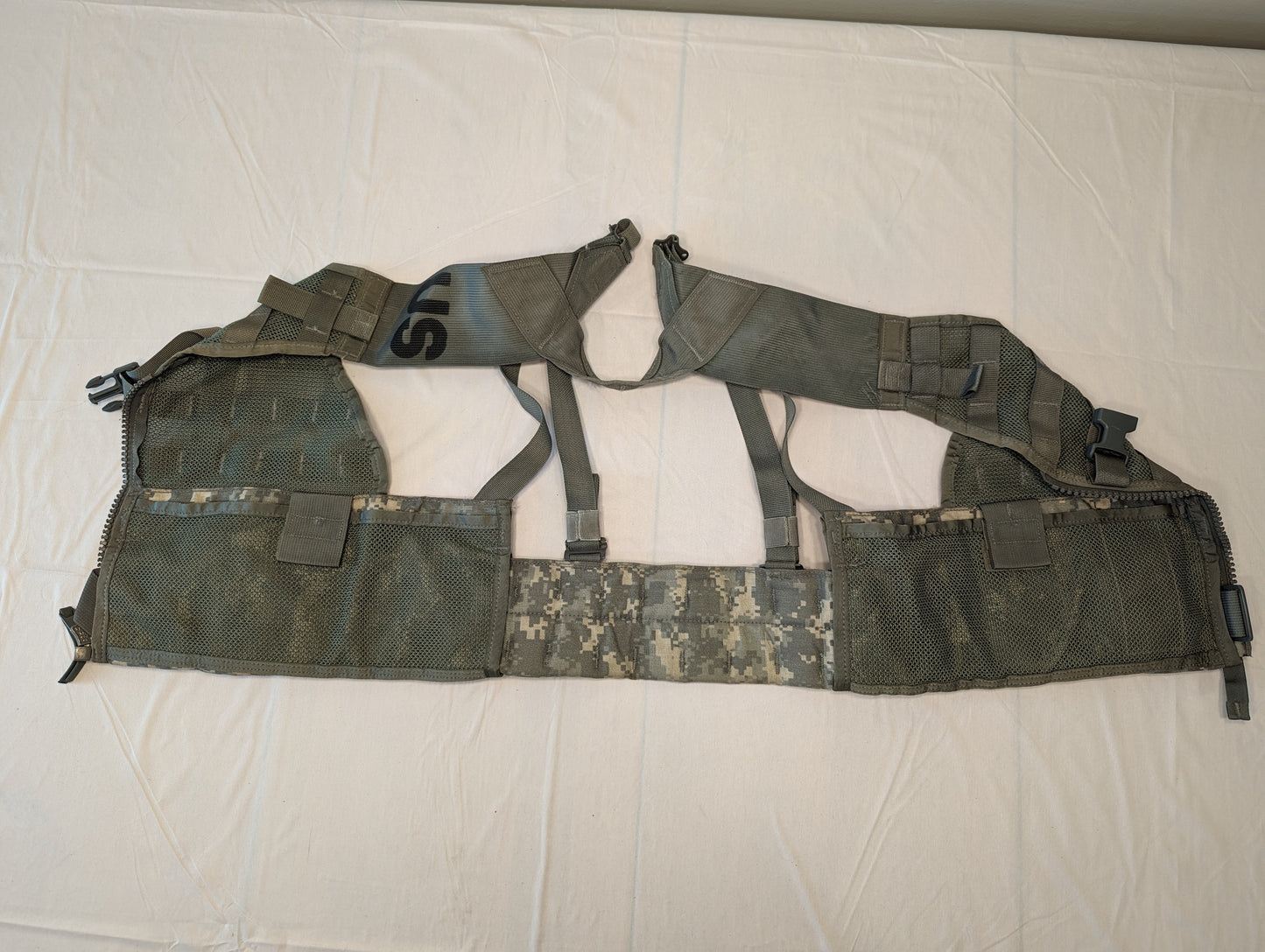 An overhead view of a U.S. Military Surplus Fighting Load Carrier (FLC) Vest in ACU digital camouflage, laid flat and fully unzipped to display the breathable mesh interior, extensive horizontal webbing, and black adjustment buckles.