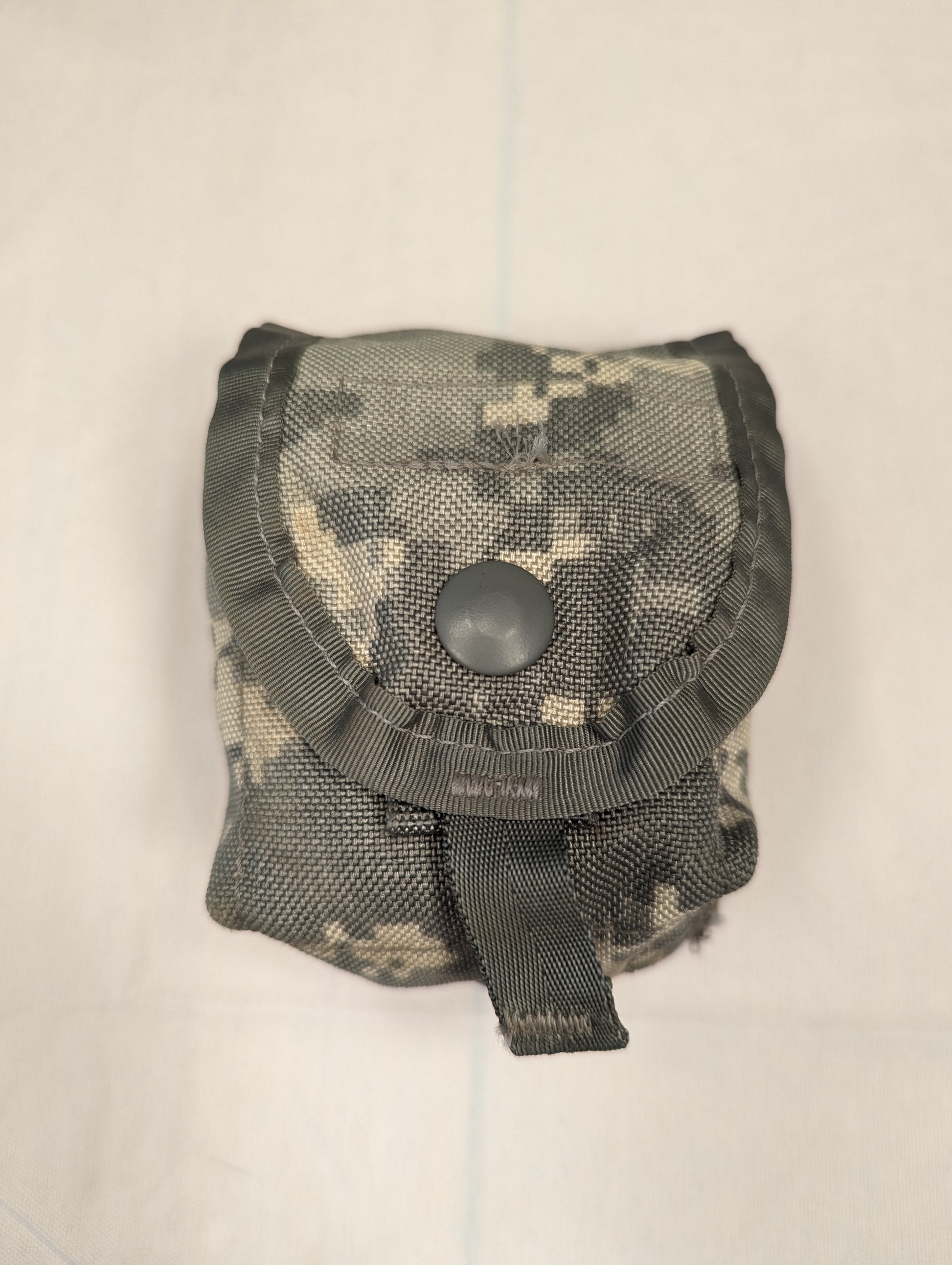 A single U.S. Military Surplus Hand Grenade Pouch in ACU digital camouflage, standing upright on a white background, featuring a snap-button flap closure and a bottom drainage loop.