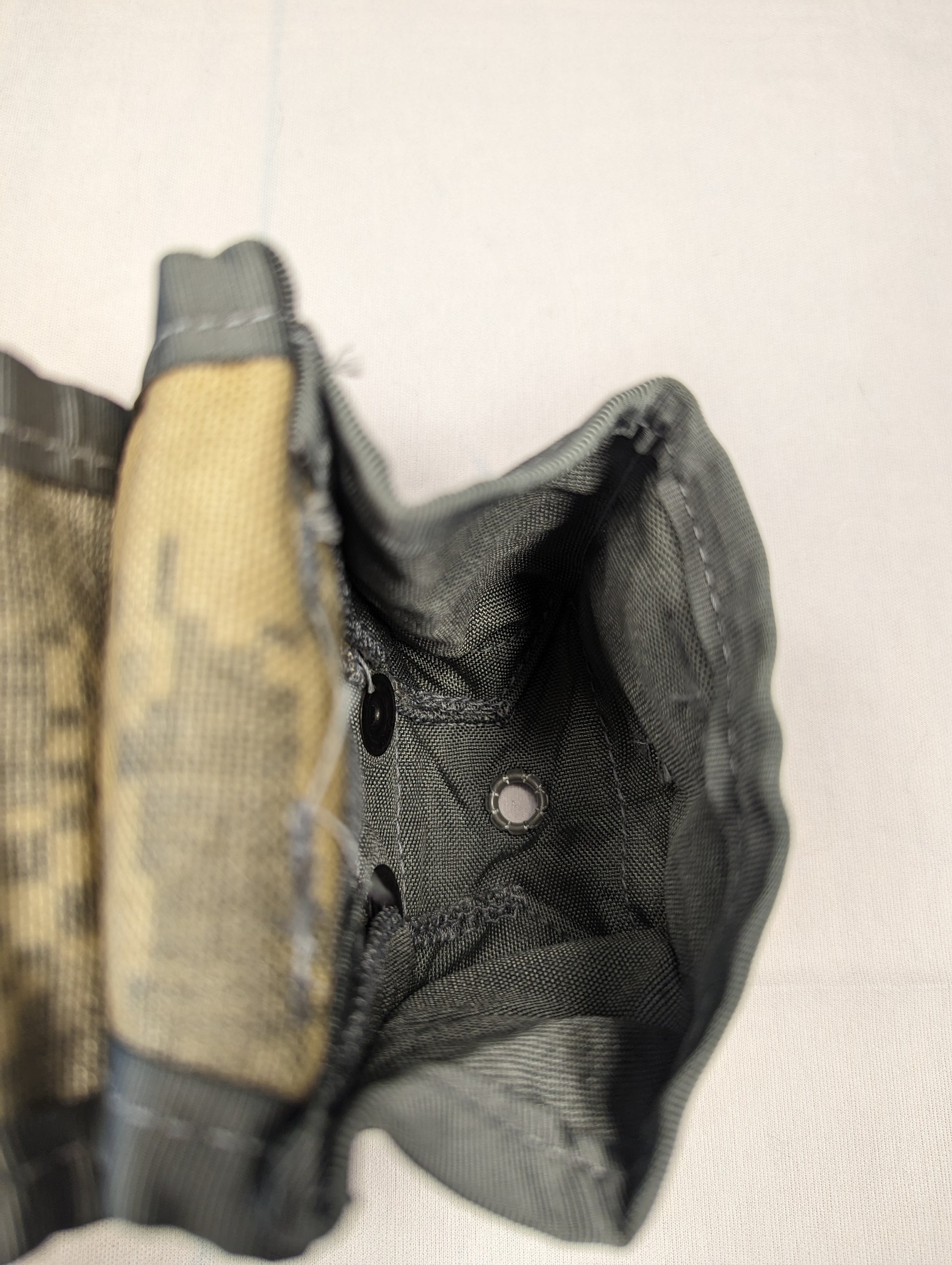 An extreme close-up view of the interior bottom of a U.S. Military Hand Grenade Pouch, highlighting the heavy stitching, dark nylon fabric, and the central drainage grommet.