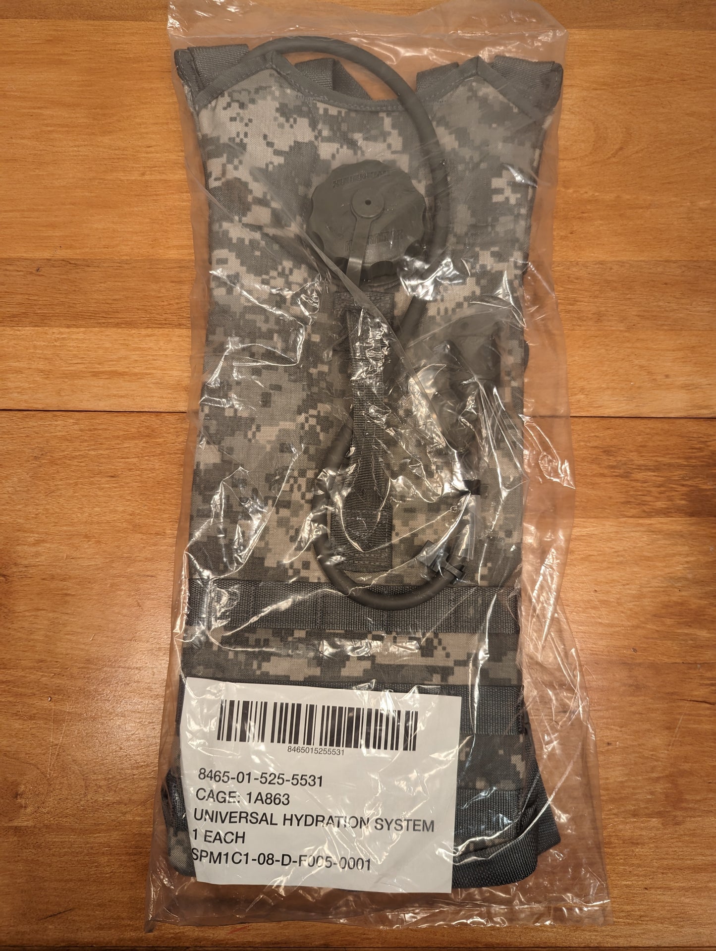 A new U.S. Military Surplus Hydration Carrier in ACU digital camouflage, sealed in plastic with a prominent issue tag displaying the NSN 8465-01-525-5531 and the product name.