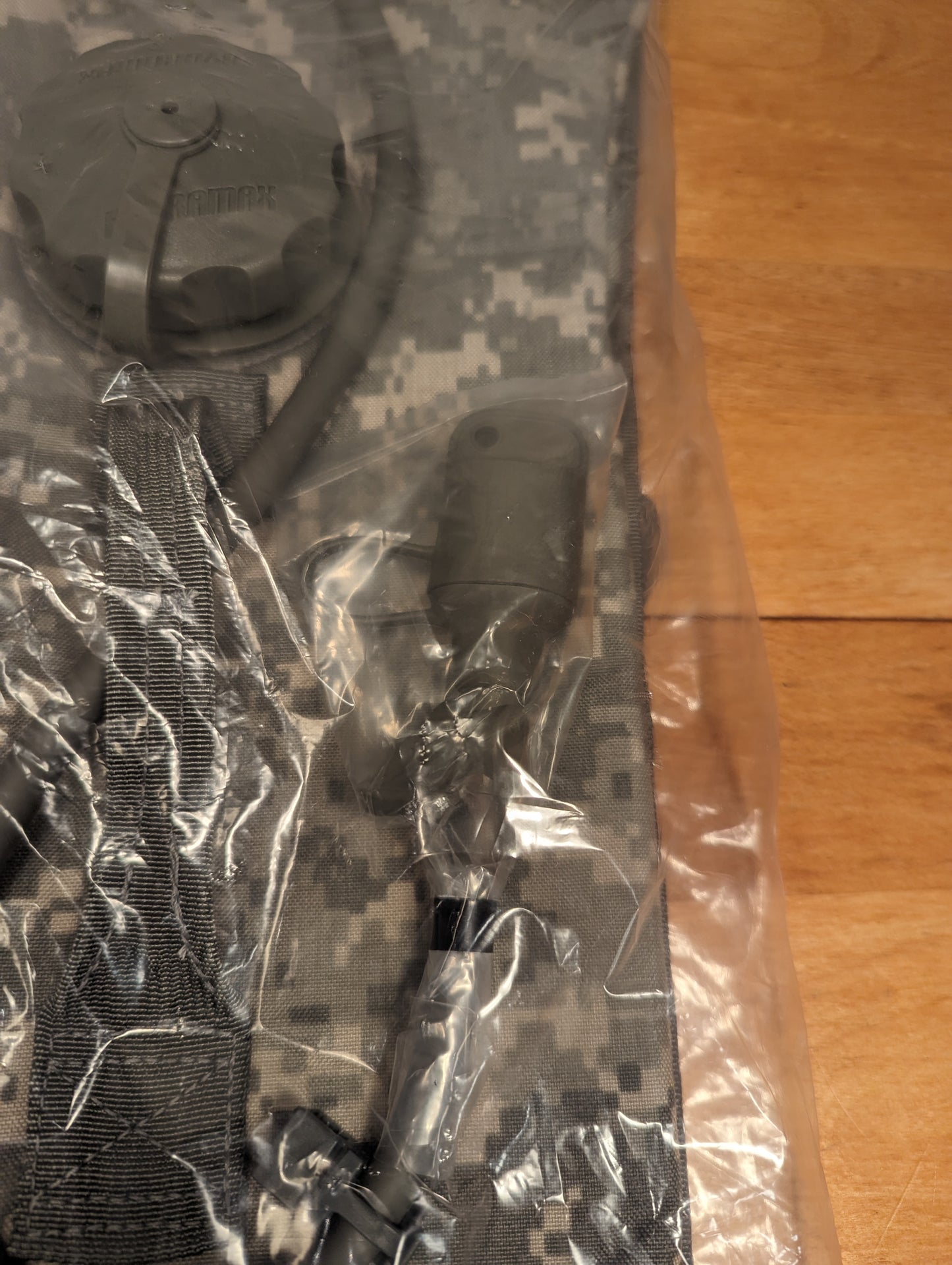 A new U.S. Military Surplus Hydration Carrier in ACU digital camouflage, sealed in clear plastic packaging, showing the cap, drinking tube, and bite valve through the plastic.