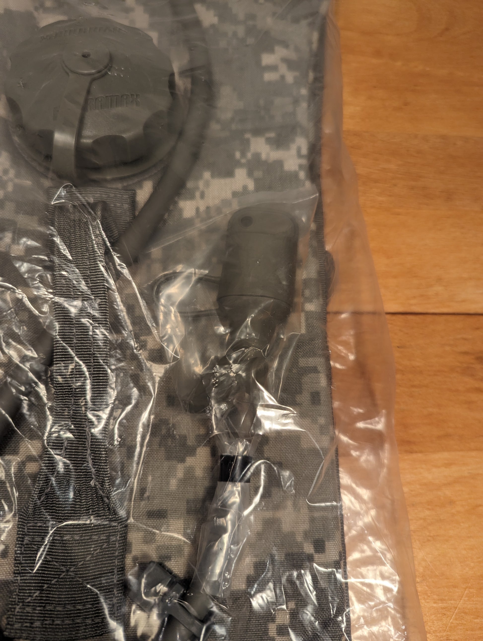 A new U.S. Military Surplus Hydration Carrier in ACU digital camouflage, sealed in clear plastic packaging, showing the cap, drinking tube, and bite valve through the plastic.