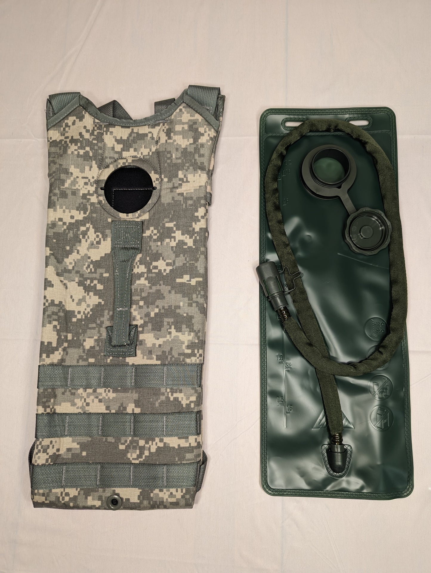 A U.S. Military Hydration System laid out, showing the ACU digital camouflage carrier shell with MOLLE webbing and the new, dark green hydration bladder and hose sealed in plastic packaging.