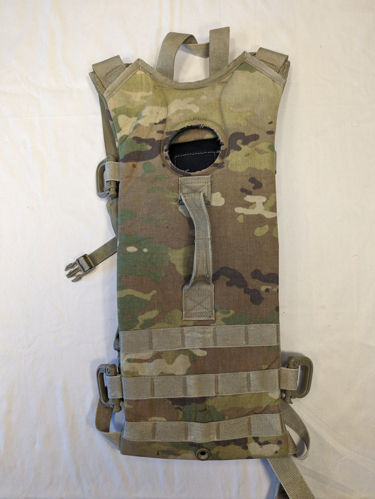 A used U.S. Military Hydration Carrier in OCP/Multicam camouflage, laid flat, showing the interior side with the structured backing, vertical MOLLE webbing, and the large top filler port opening.