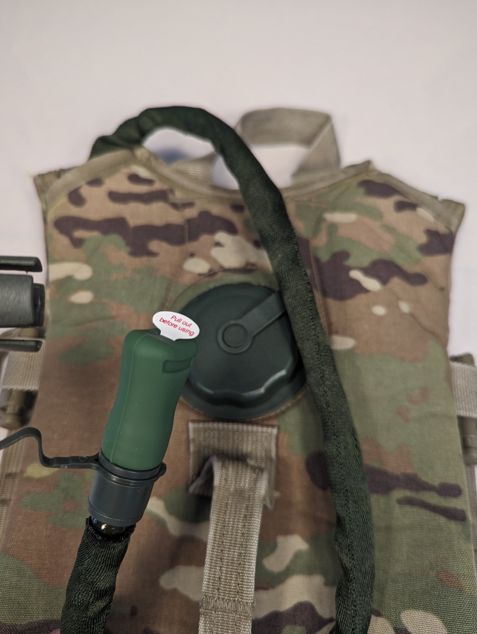 A close-up of a used OCP/Multicam Hydration Carrier, featuring the newly installed black filler cap and insulated drinking hose attached to the camouflage pack shell.