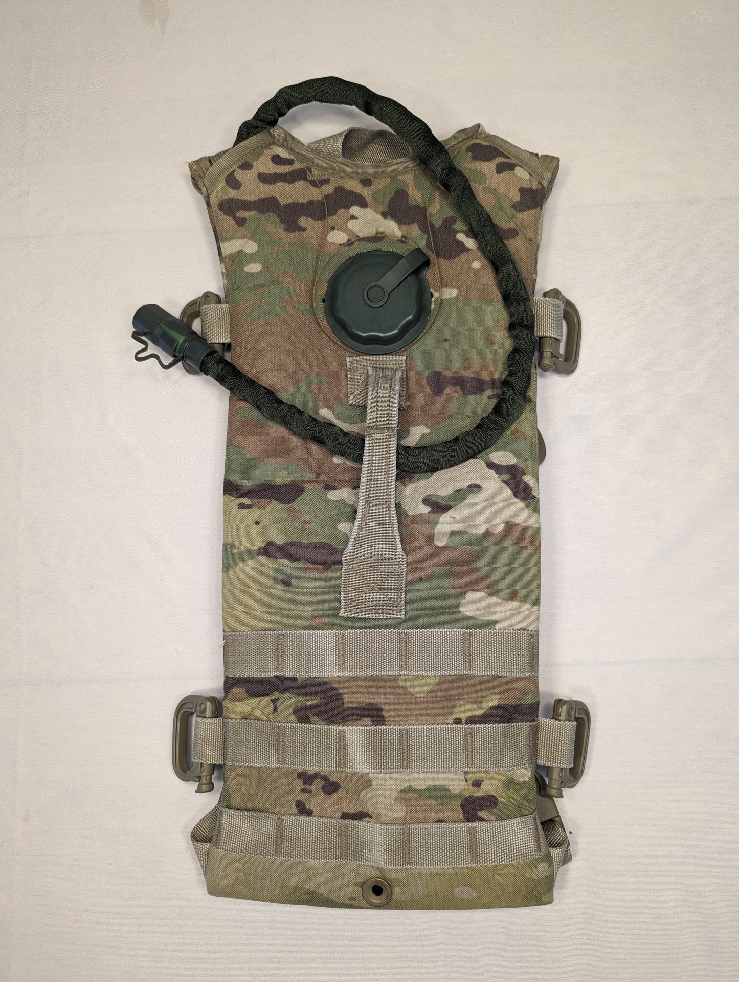 A used U.S. Military Hydration Carrier in OCP/Multicam camouflage, featuring horizontal MOLLE webbing and a brand new black bladder hose and filler cap draped over the front.