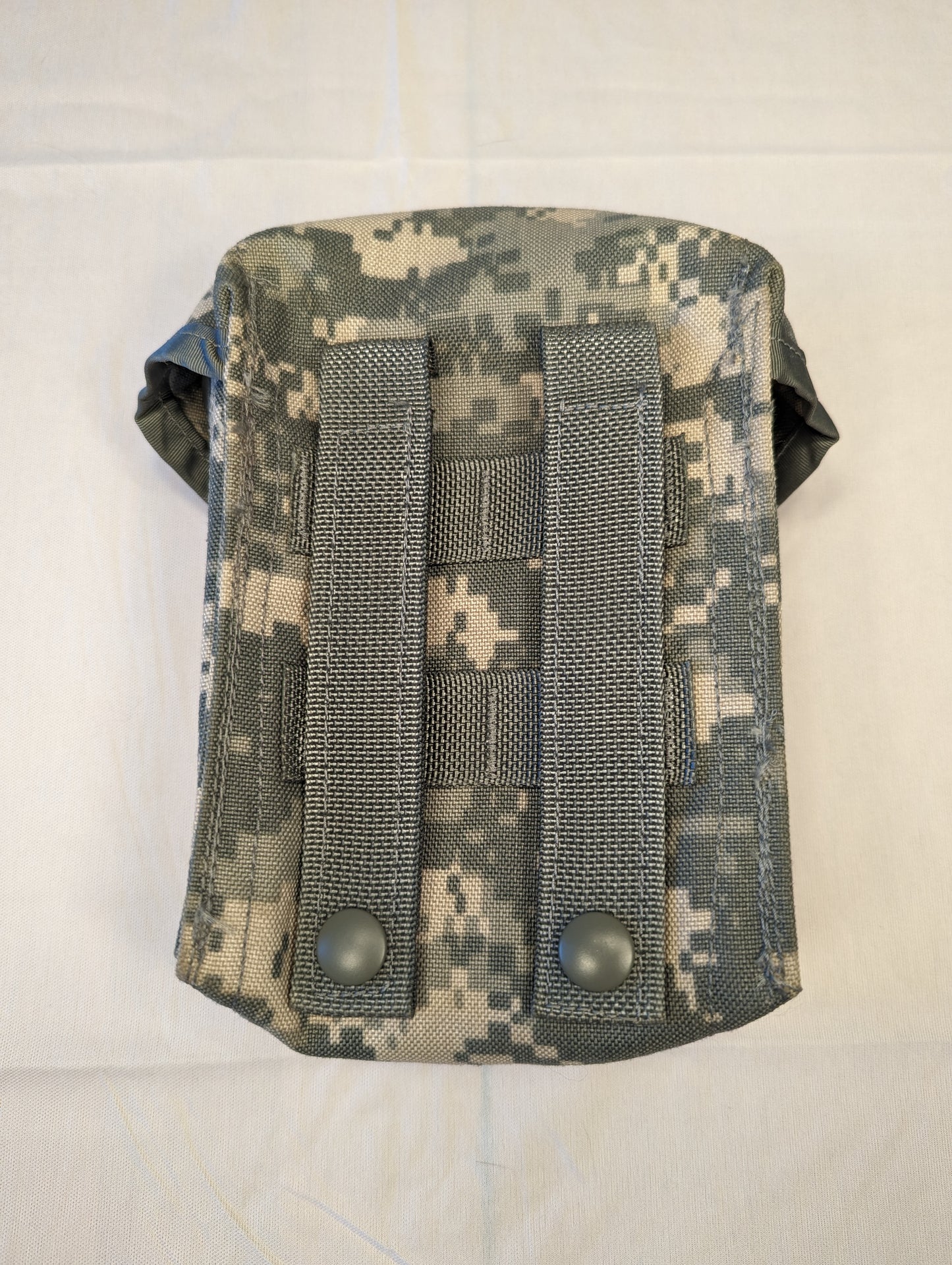 A close-up back view of a U.S. Military Surplus Improved First Aid Kit (IFAK) Pouch in ACU digital camouflage, featuring two foliage green MOLLE attachment straps with metal snap closures.
