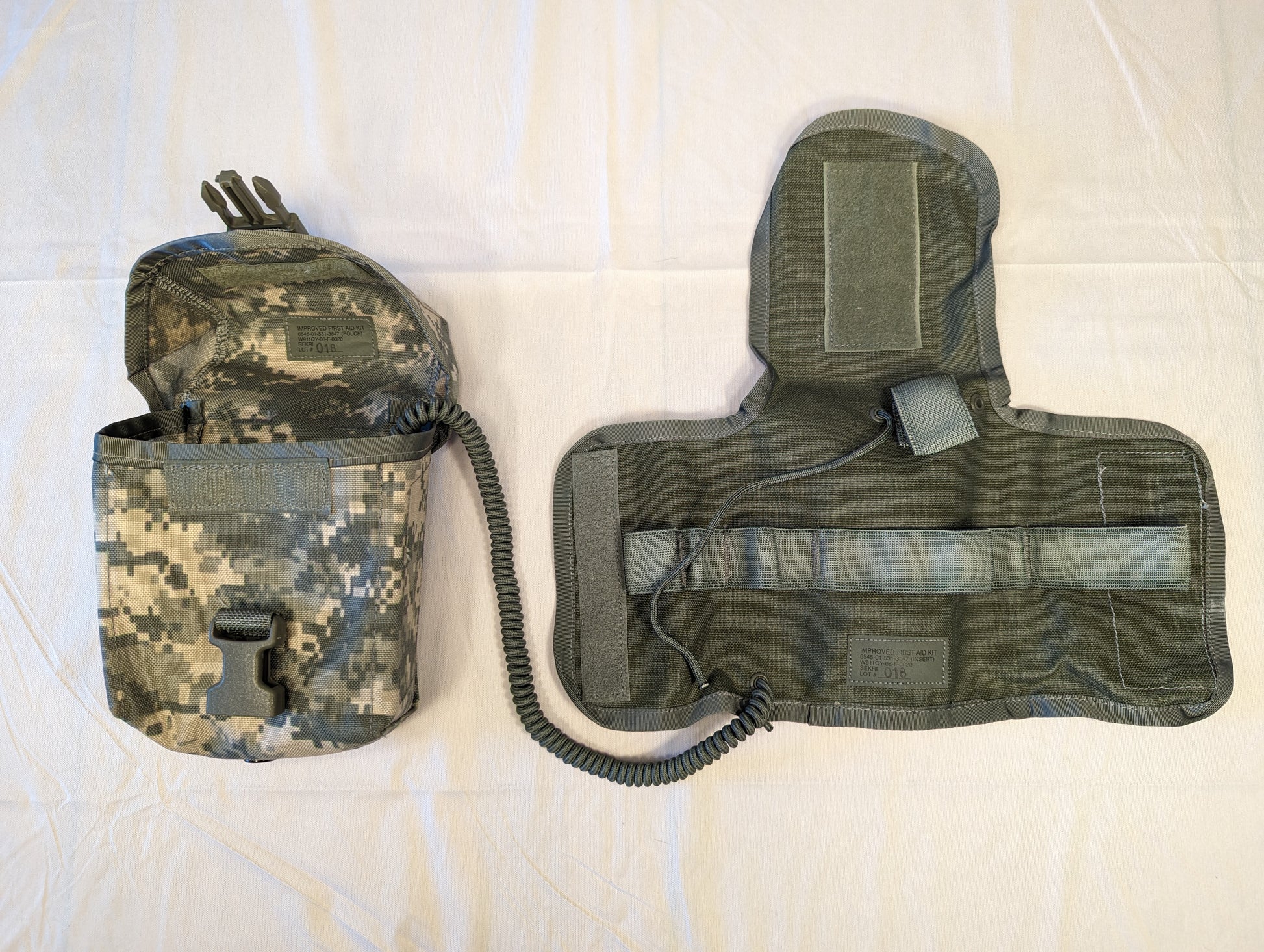 A U.S. Military Surplus Individual First Aid Kit (IFAK) laid open, showing the UCP/ACU camouflage outer pouch and the internal olive green tri-fold insert with empty elastic organizational loops.