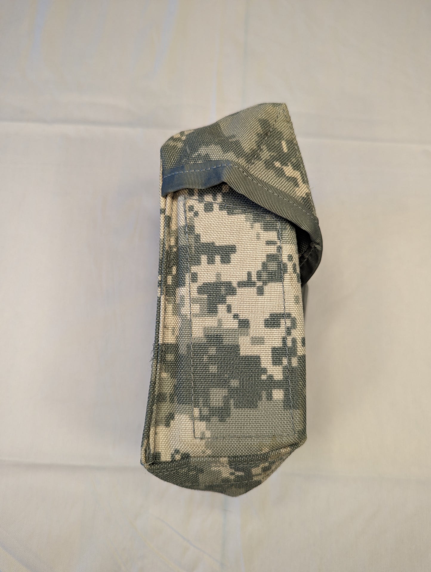 A single U.S. Military Surplus Individual First Aid Kit (IFAK) pouch in UCP/ACU digital camouflage, standing upright and closed with a black quick-release buckle and vertical webbing strap.
