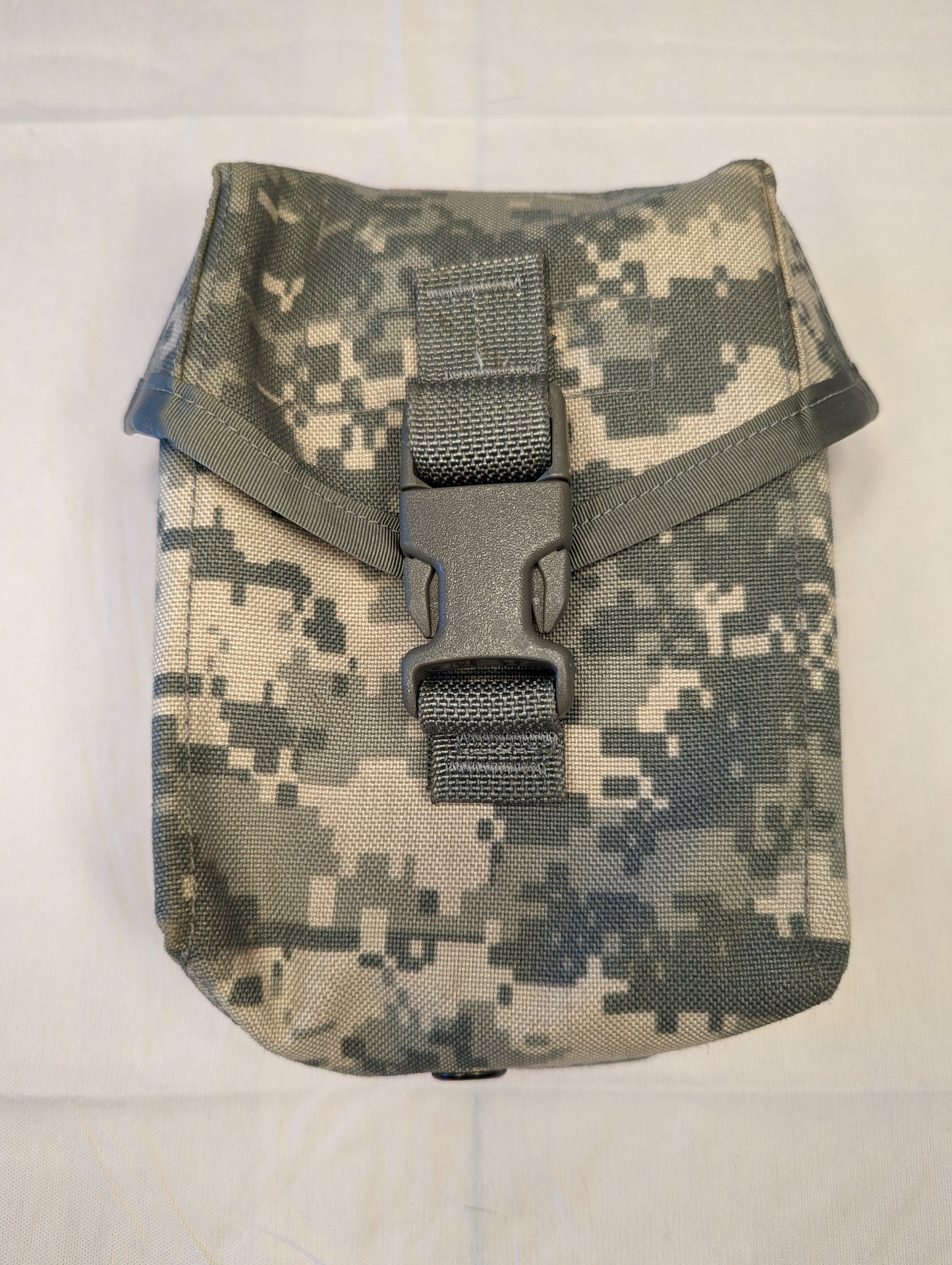 A single U.S. Military Surplus Individual First Aid Kit (IFAK) pouch in UCP/ACU digital camouflage, standing upright and closed with a black quick-release buckle and vertical webbing strap.