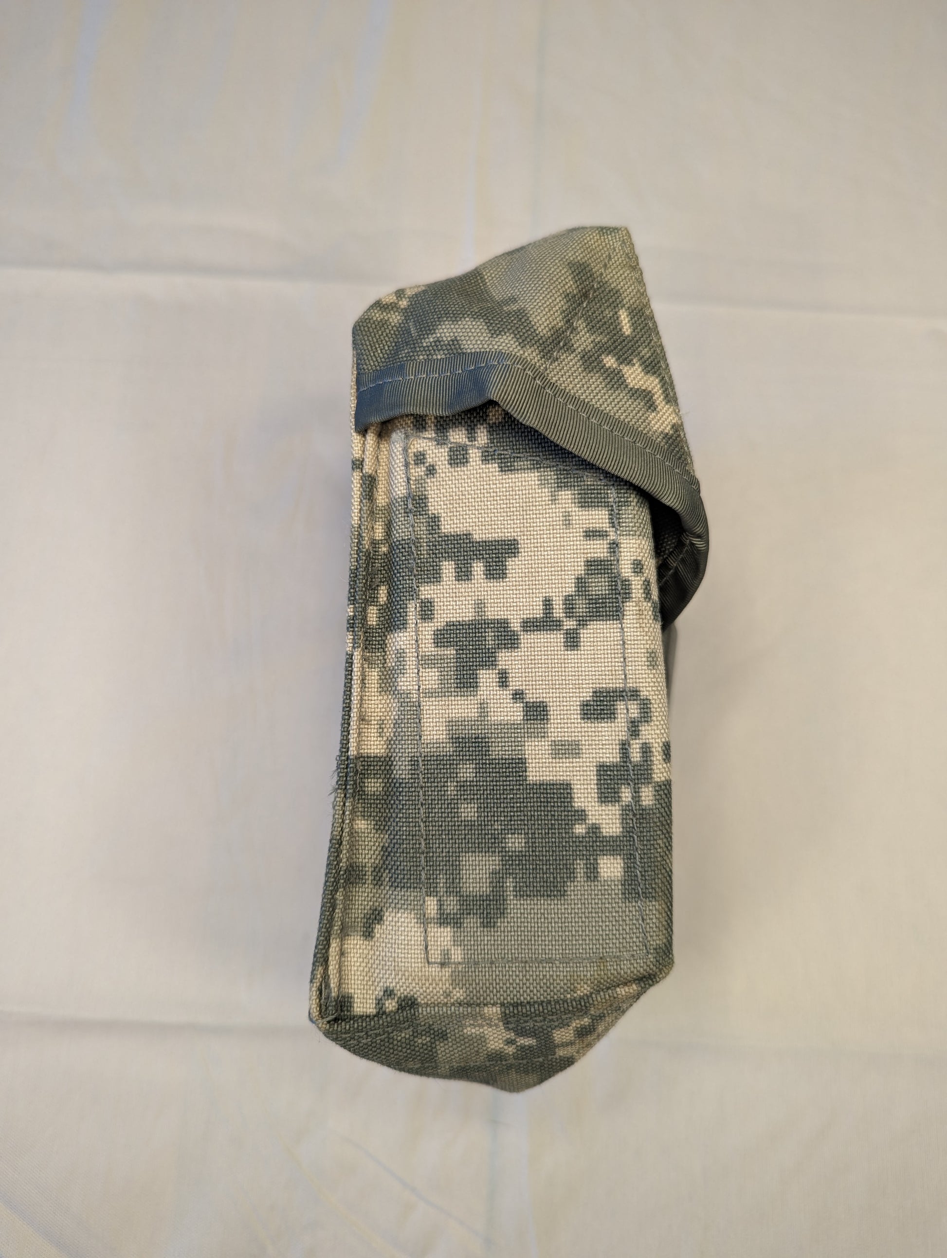 A single U.S. Military Surplus Improved First Aid Kit (IFAK) pouch in ACU digital camouflage, packed tightly into a vertical cylinder and secured with a top flap closure, displayed on a white background.