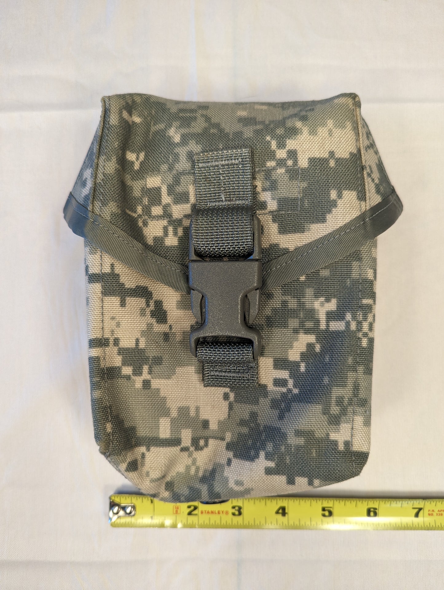 A single U.S. Military Surplus Individual First Aid Kit (IFAK) Pouch in ACU digital camouflage, laid flat with a tape measure demonstrating its width of approximately 7 inches, and secured by a black quick-release buckle.
