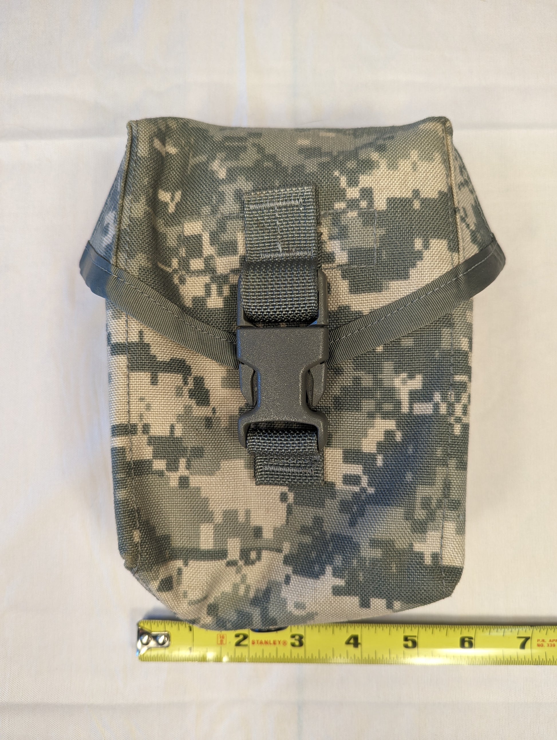 A single U.S. Military Surplus Individual First Aid Kit (IFAK) Pouch in ACU digital camouflage, laid flat with a tape measure demonstrating its width of approximately 7 inches, and secured by a black quick-release buckle.