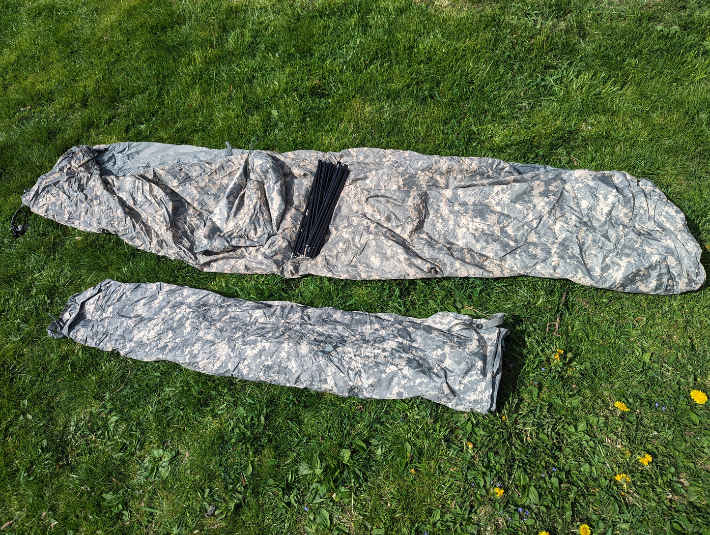 The U.S. Military Improved Combat Shelter (ICS) broken down into two components (main tent and stuff sack) and rolled in ACU digital camouflage, laid out on a green grass background.