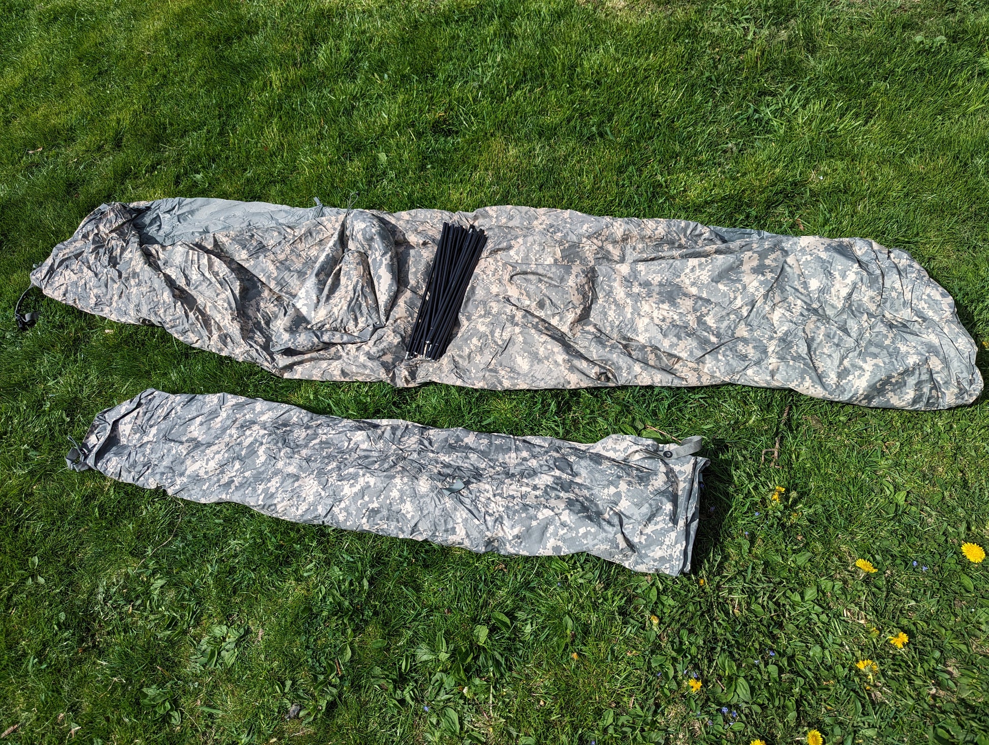 The U.S. Military Improved Combat Shelter (ICS) broken down into two components (main tent and stuff sack) and rolled in ACU digital camouflage, laid out on a green grass background.
