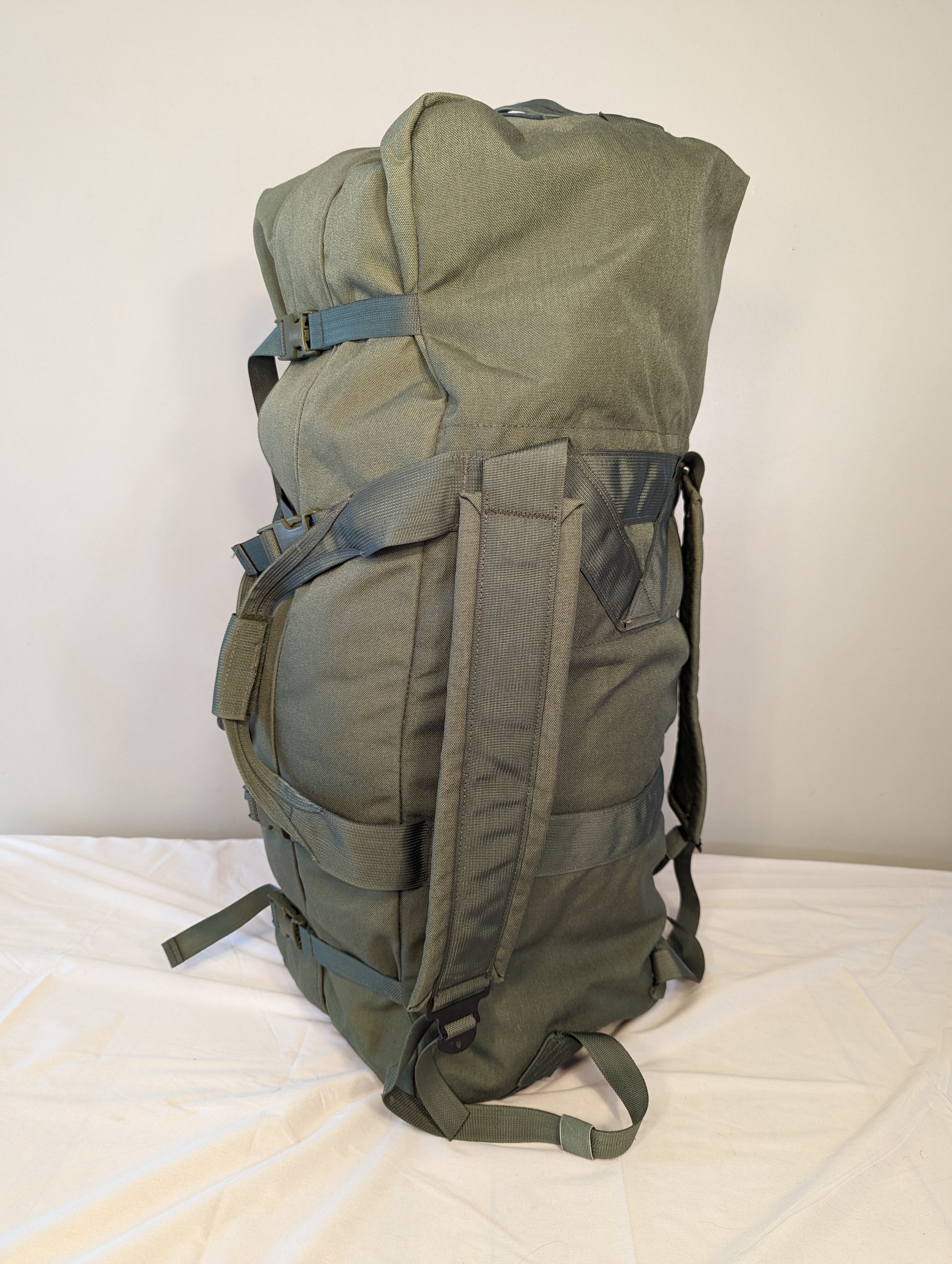 A large U.S. Military Surplus Improved Duffel Bag (IDB) in olive green, standing upright, featuring heavy-duty webbing, compression straps.